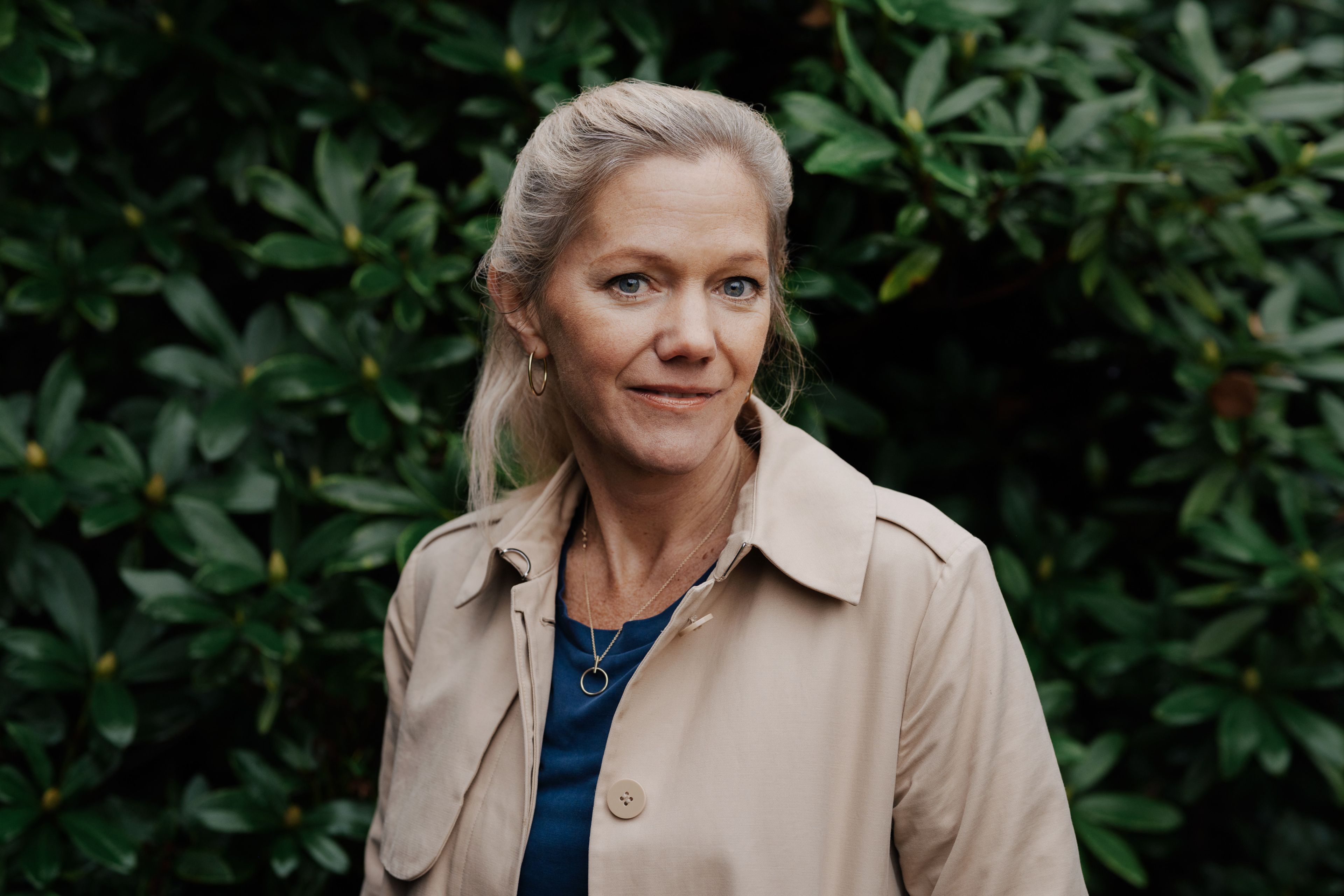 Liggende portrettfoto av Maja Lunde. I bakgrunnen er det en grønn hekk.