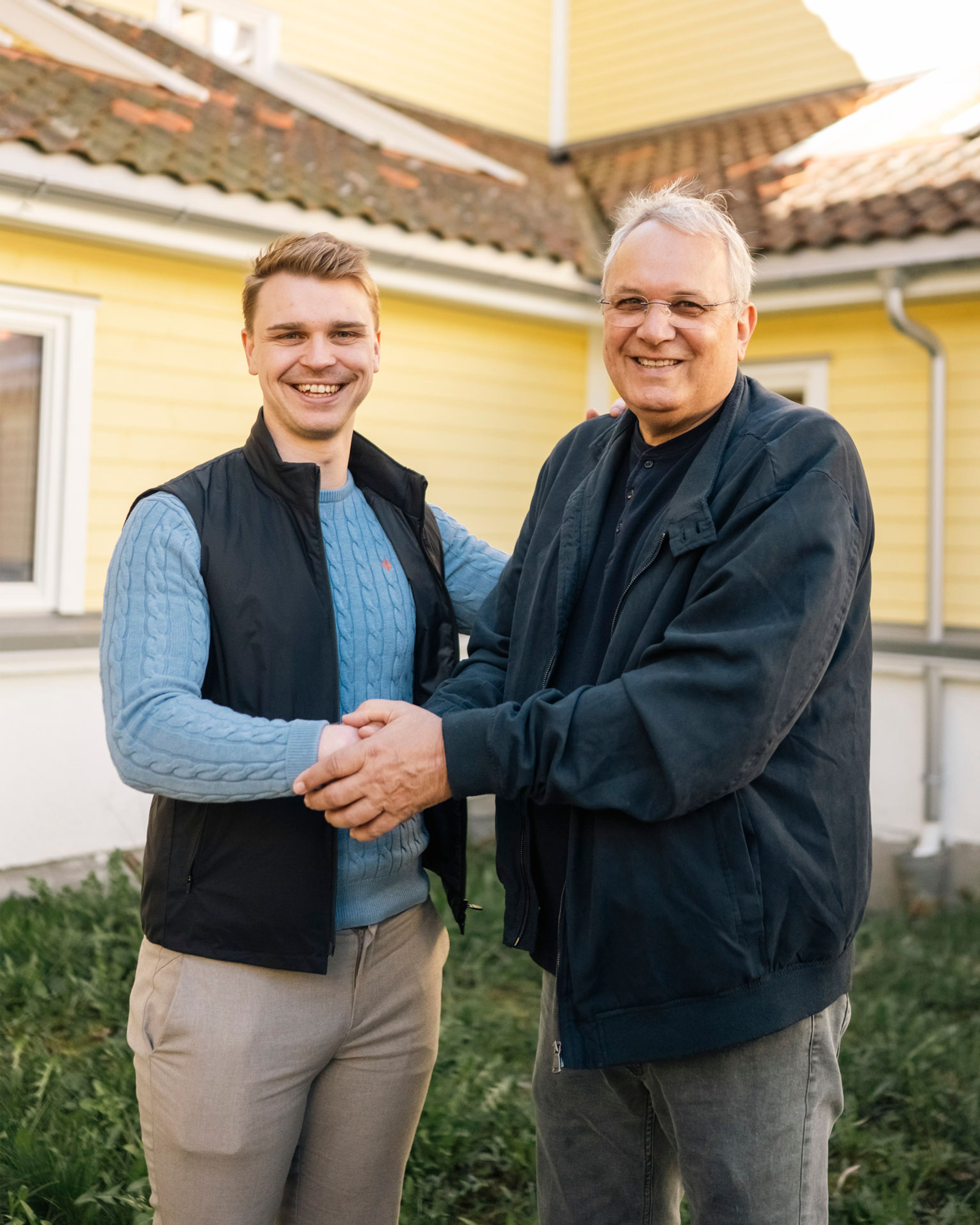 Rådgiver Eirik Karlsen og styreleder Olav Berger håndhilser og smiler foran den gule trefasaden på Holmen borettslag.