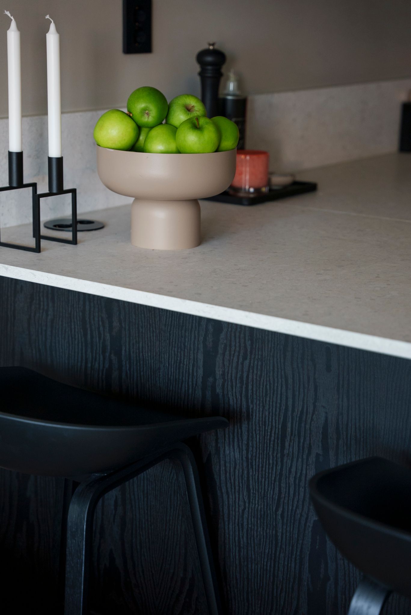 Detaljbilde av et sort kjøkken med lys benkeplate med en skål med grønne epler på