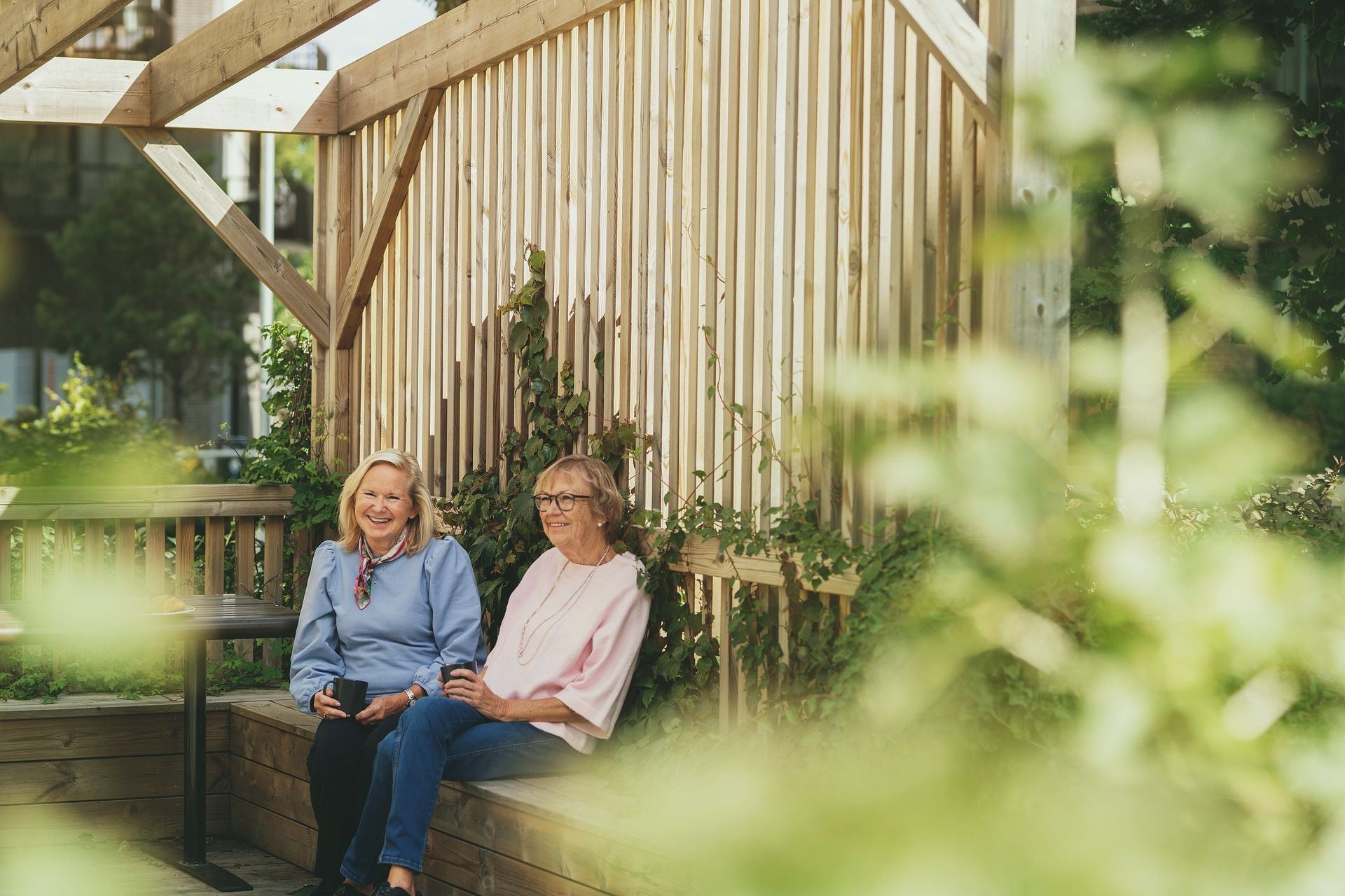 To kvinner sitter på en benk i bakgården i et borettslag