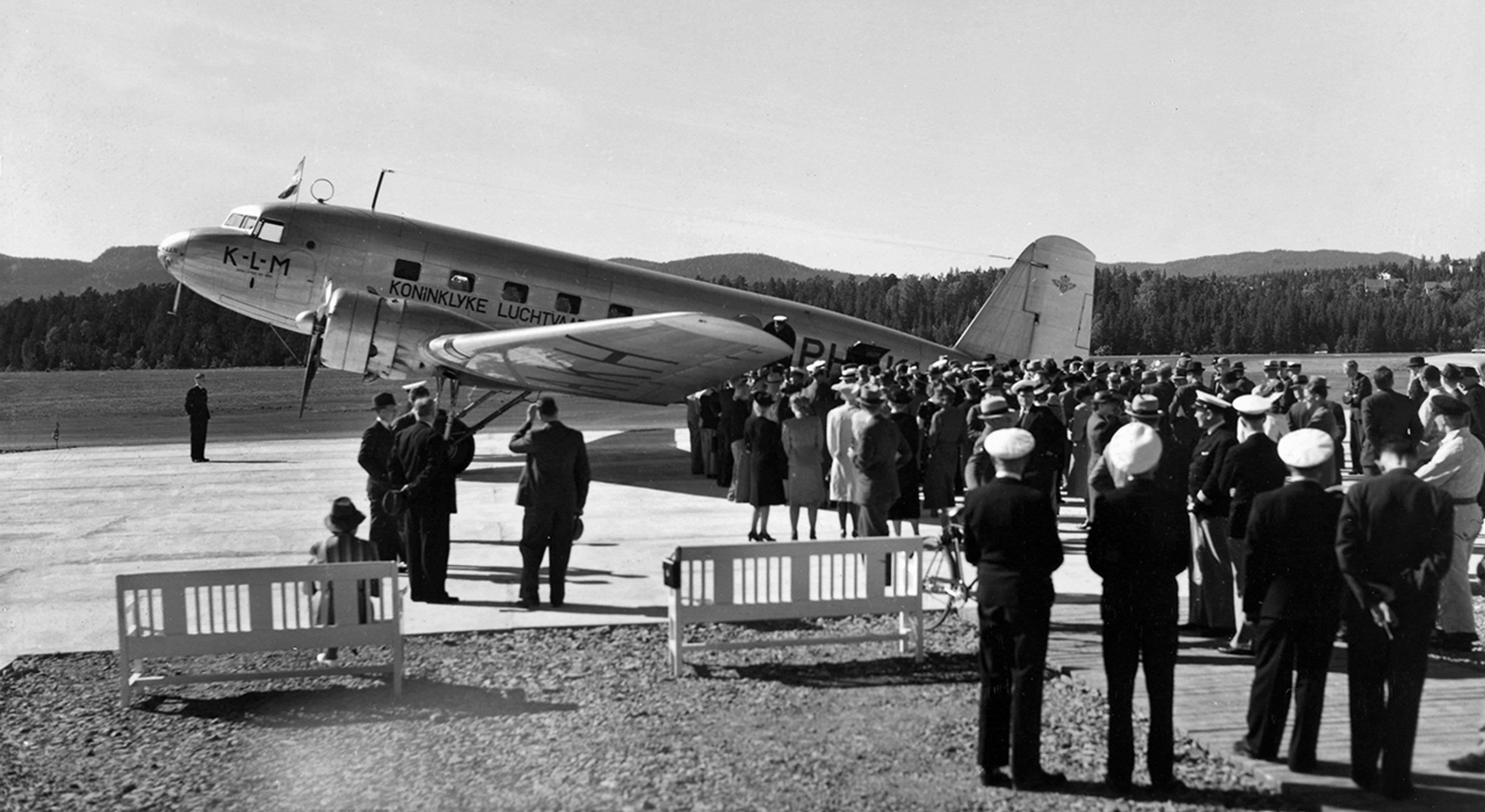 Svart-hvitt bilde av en folkemengde på en rullebane ved et fly.