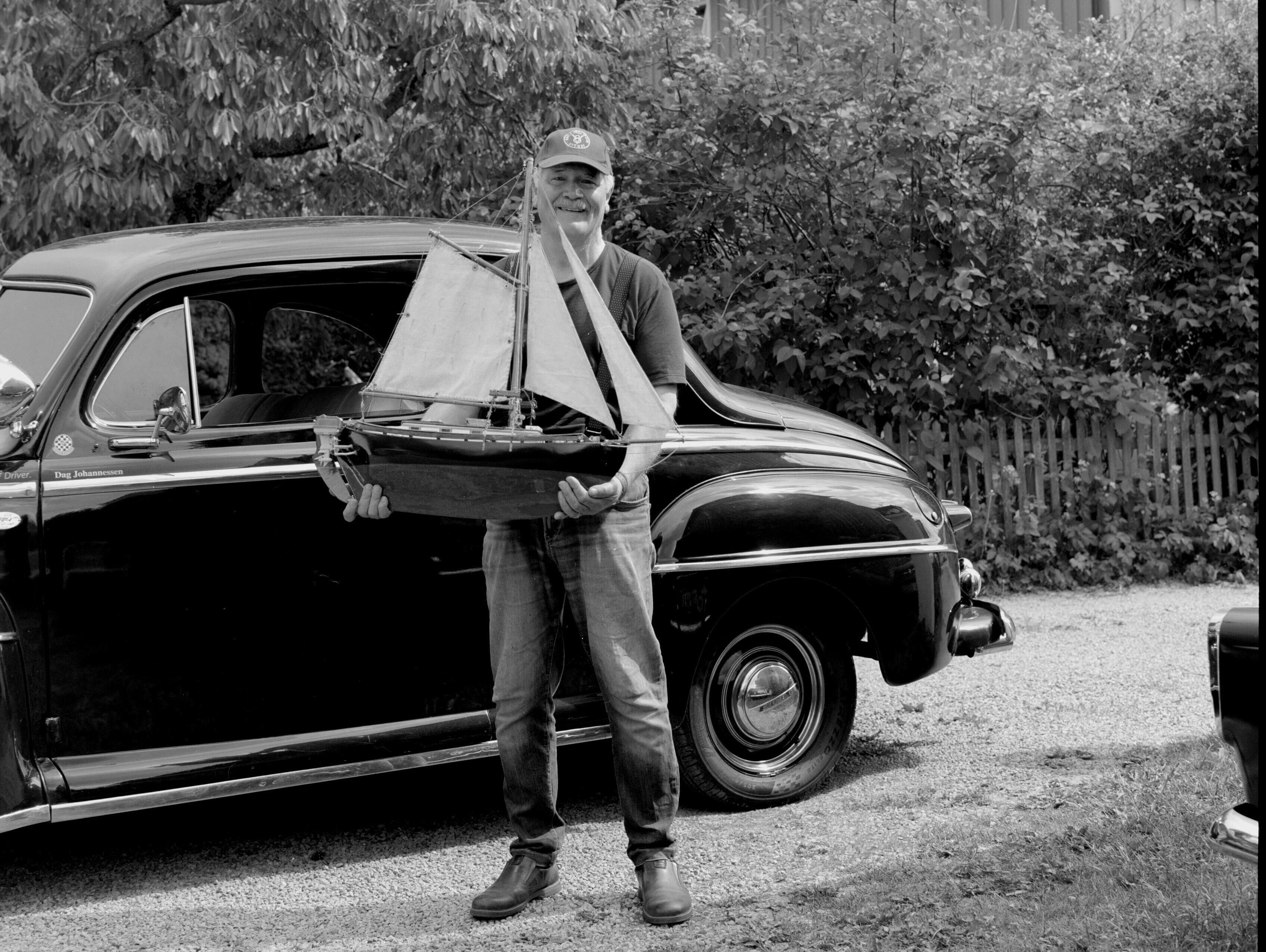 Thormod står foran en av veteranbilene sine og holder en modellbåt i armene.