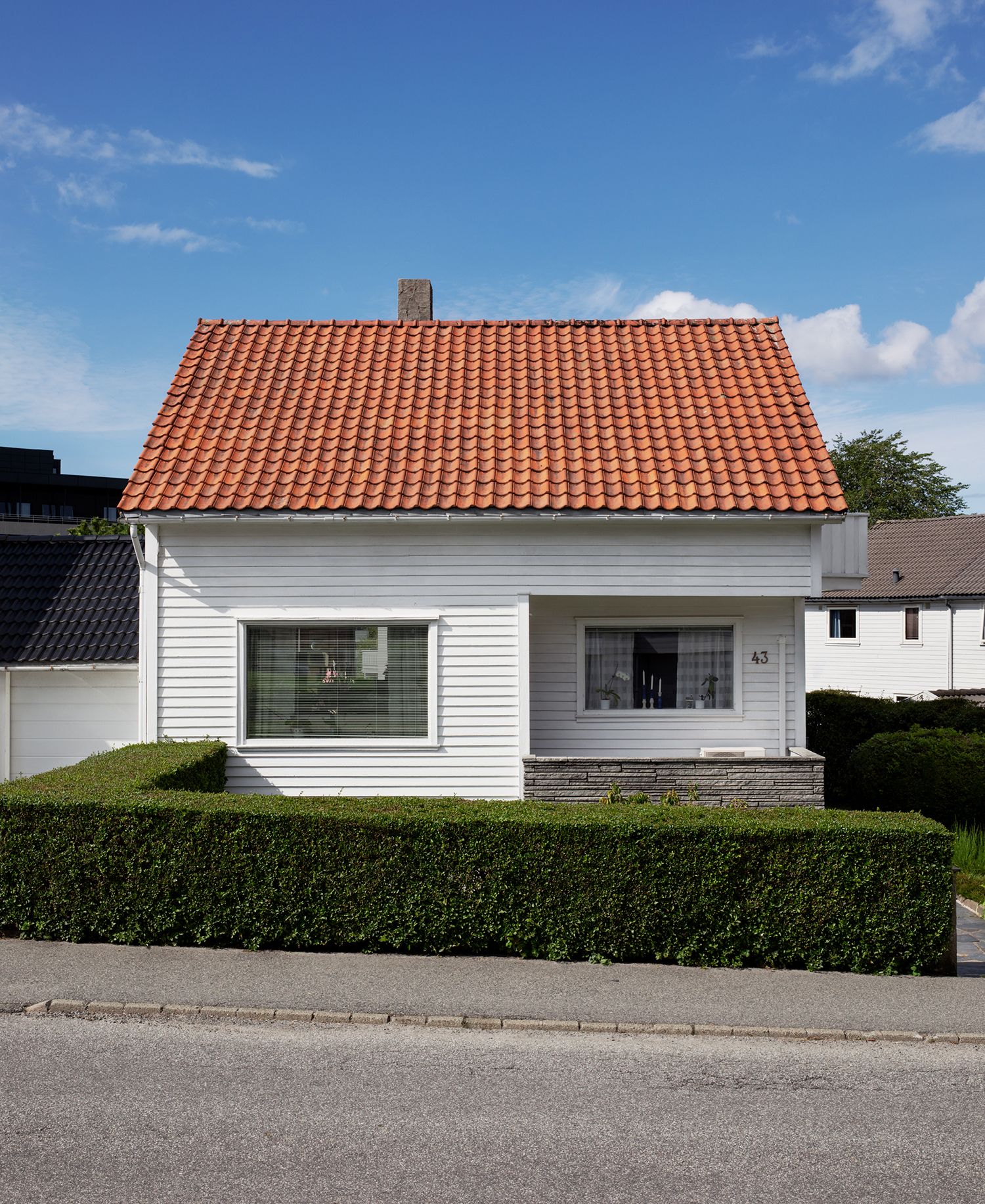 Et hvitt Block Watne-hus med rødt tak og grønn hekk foran.