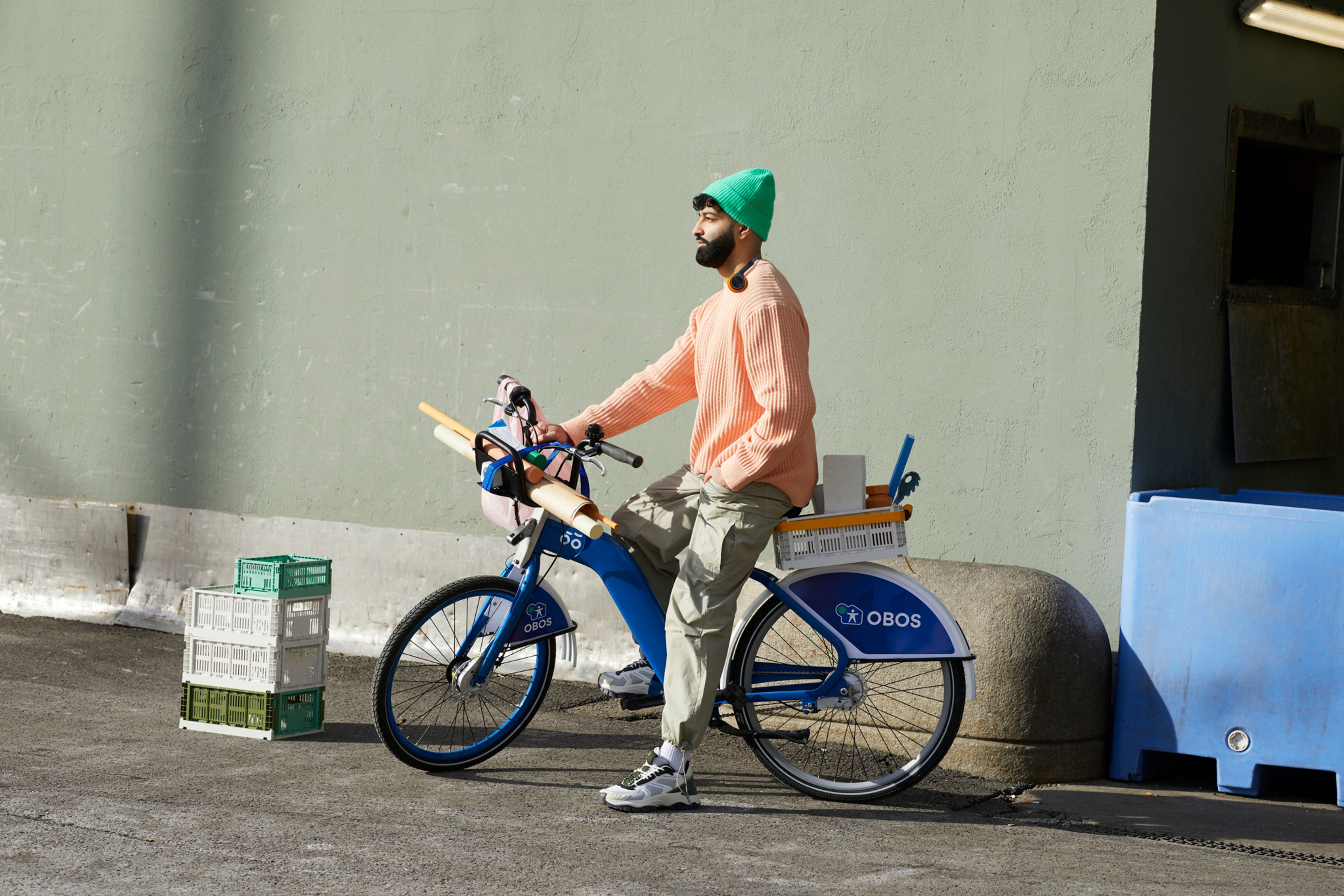 En mann på en bysykkel med fargerike klær. Sykkelen er lastet med ulike interiørting og ruller med papir.