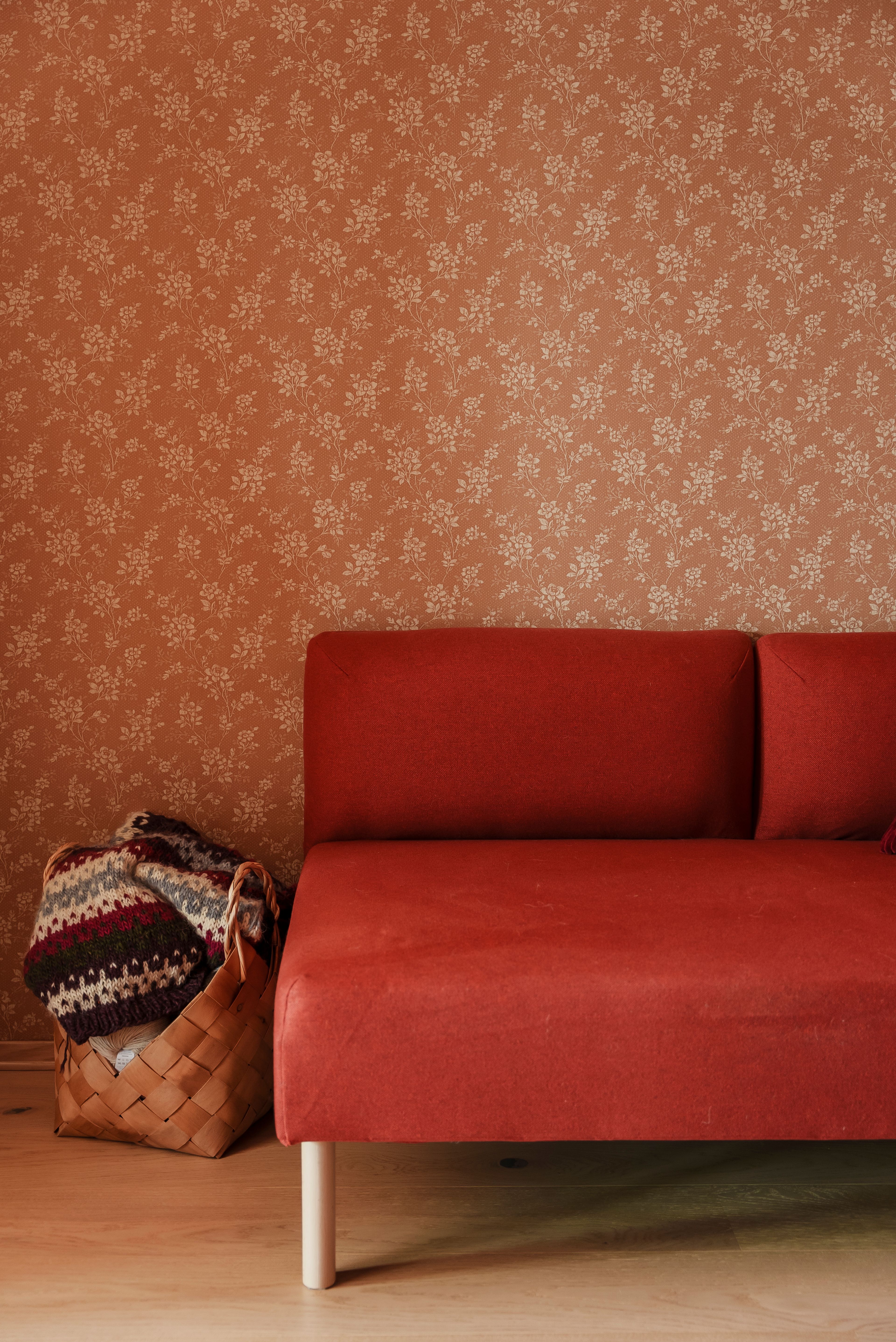 Nærbilde av en rød sofa mot en brun tapetsert vegg med blomstermønster.