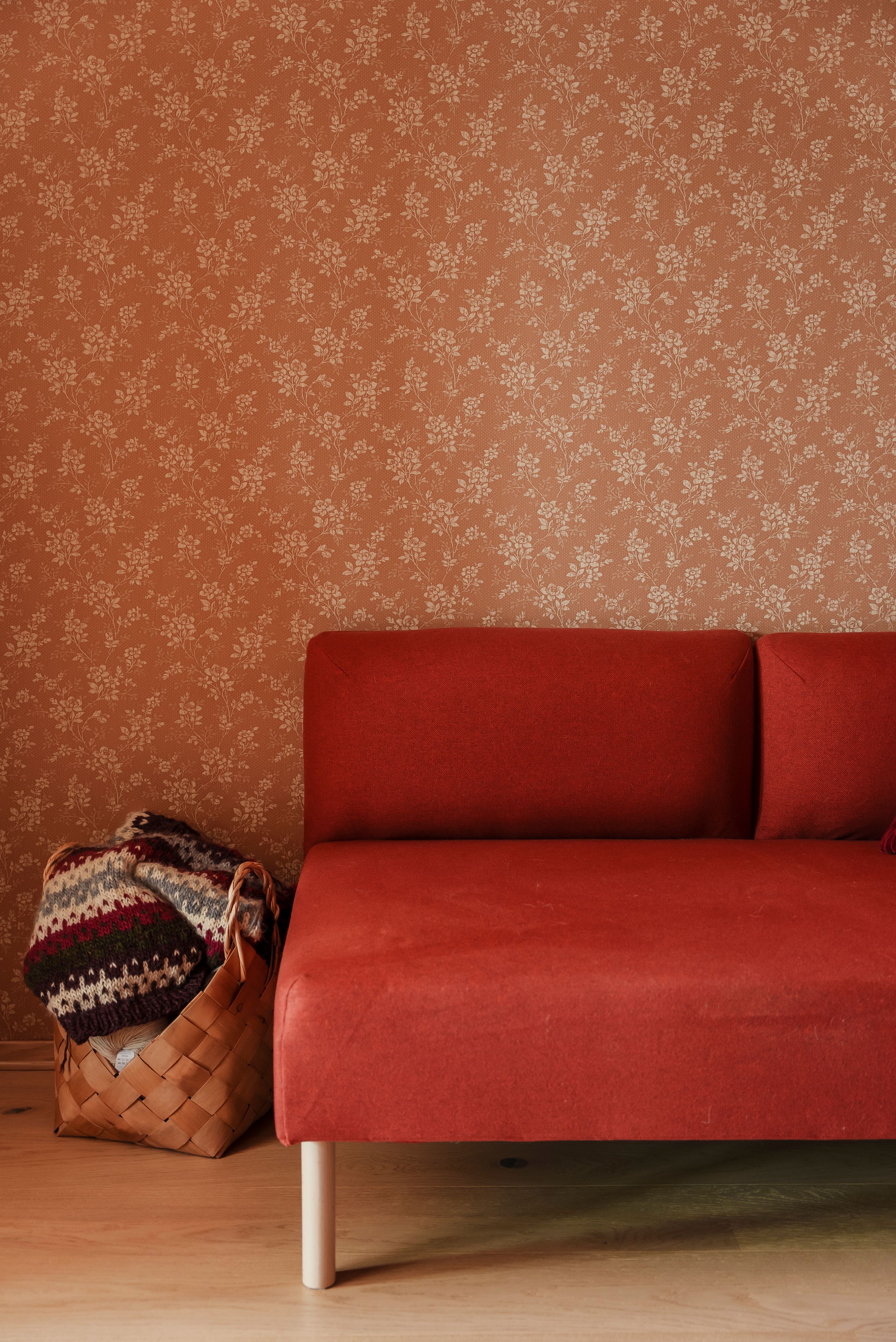 Nærbilde av en rød sofa mot en brun tapetsert vegg med blomstermønster.
