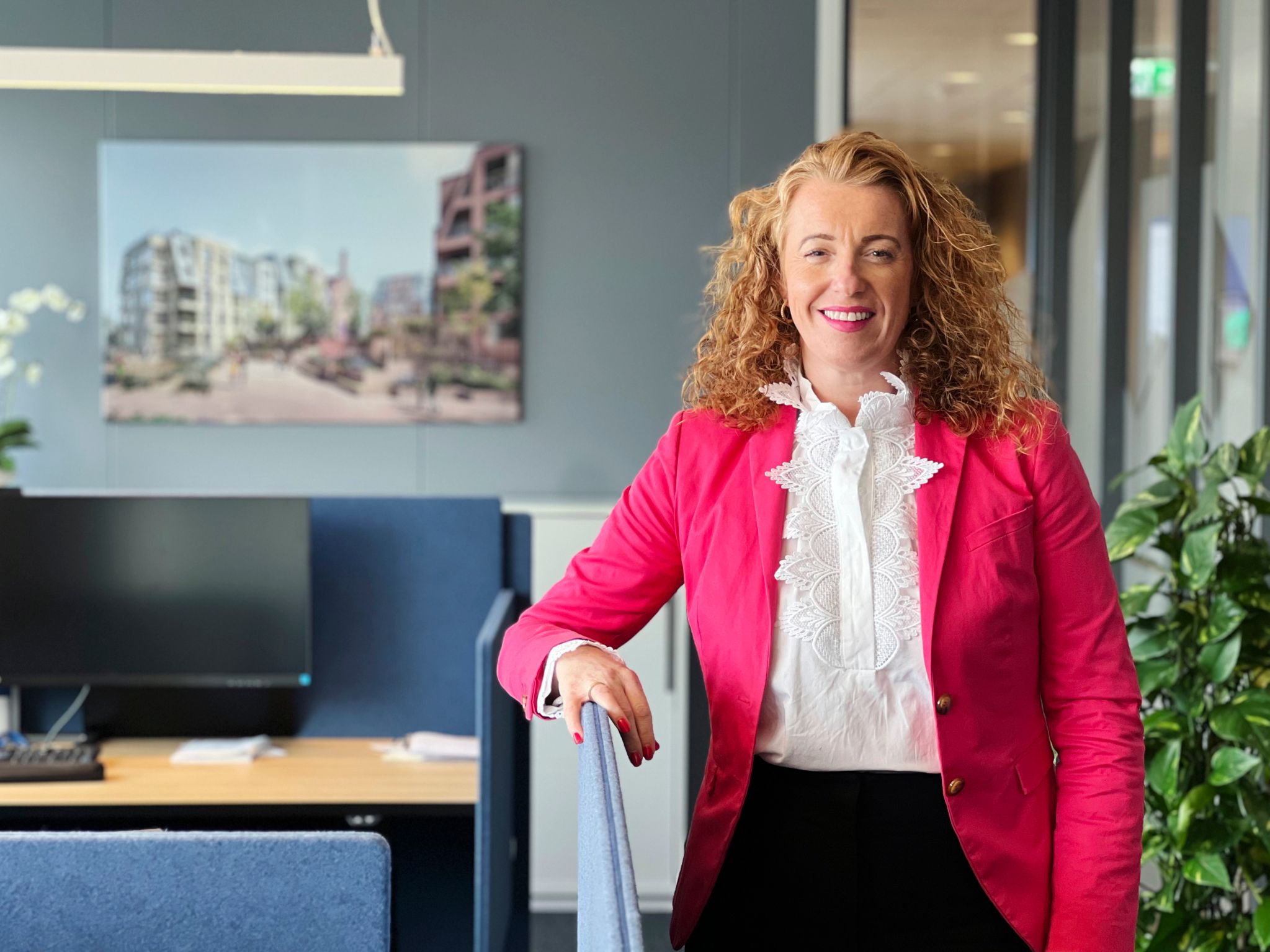 Kristin står på et kontor og lener armen på en av skilleveggene mellom plassene i et åpent kontorlandskap.