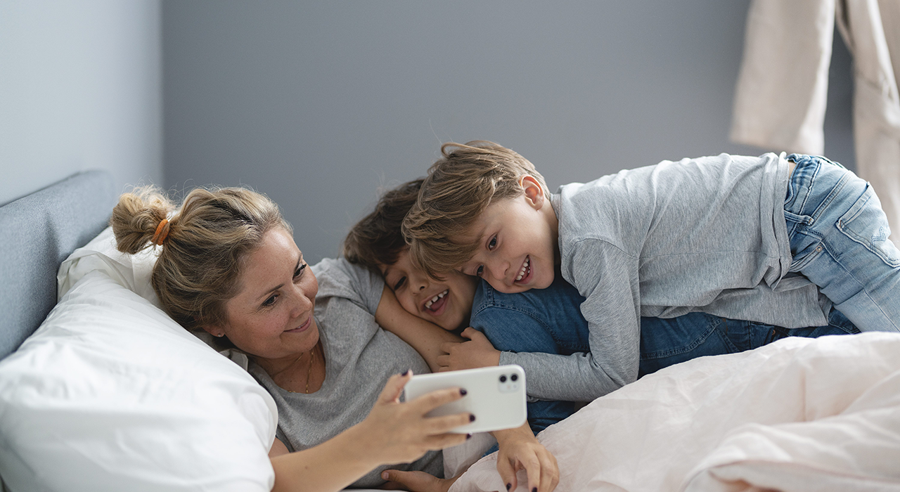a woman is laying on a bed with two children looking at a cell phone