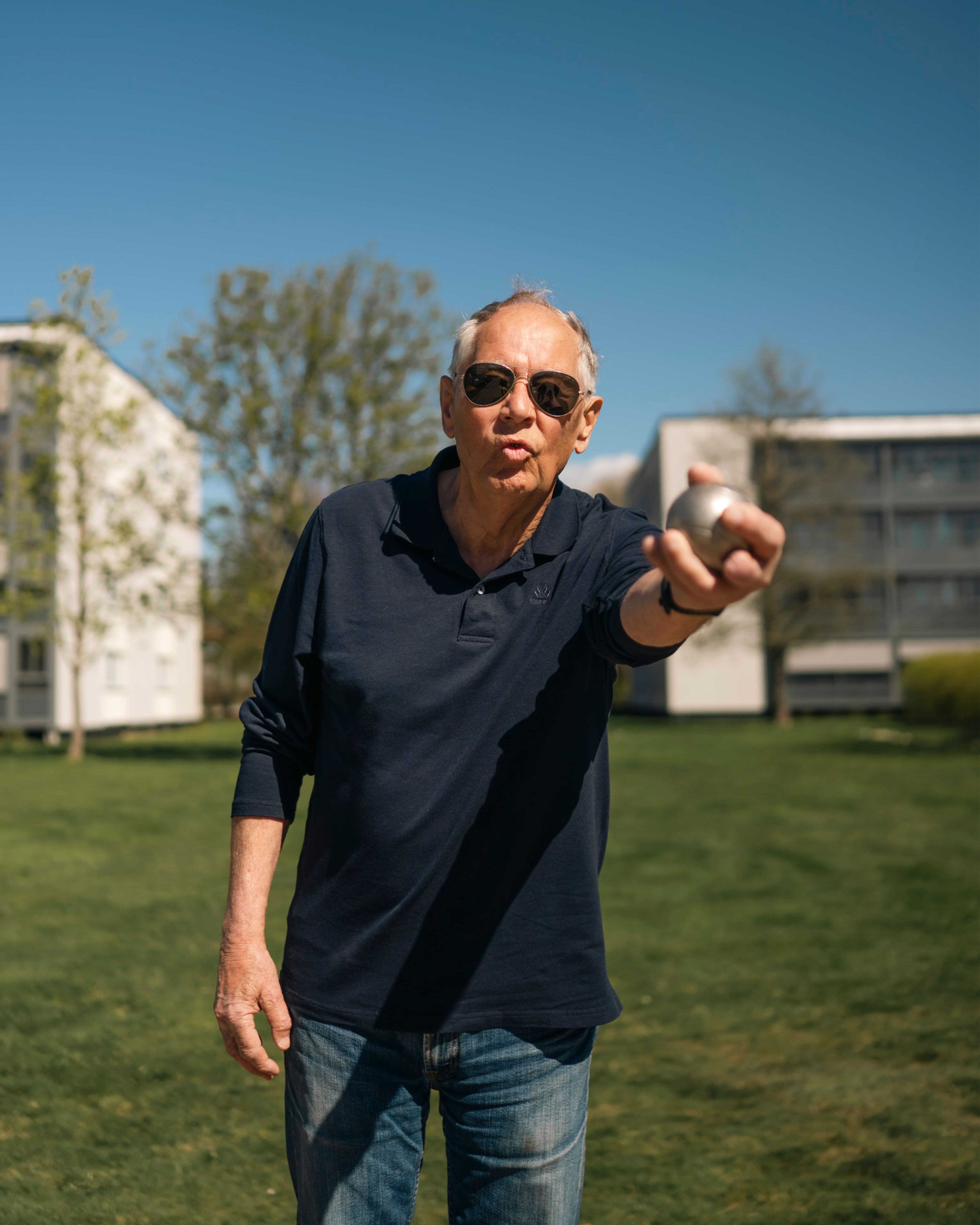 Eldre mann spiller petanque på gressplen i et boligområde og kaster en kule mot kamera.