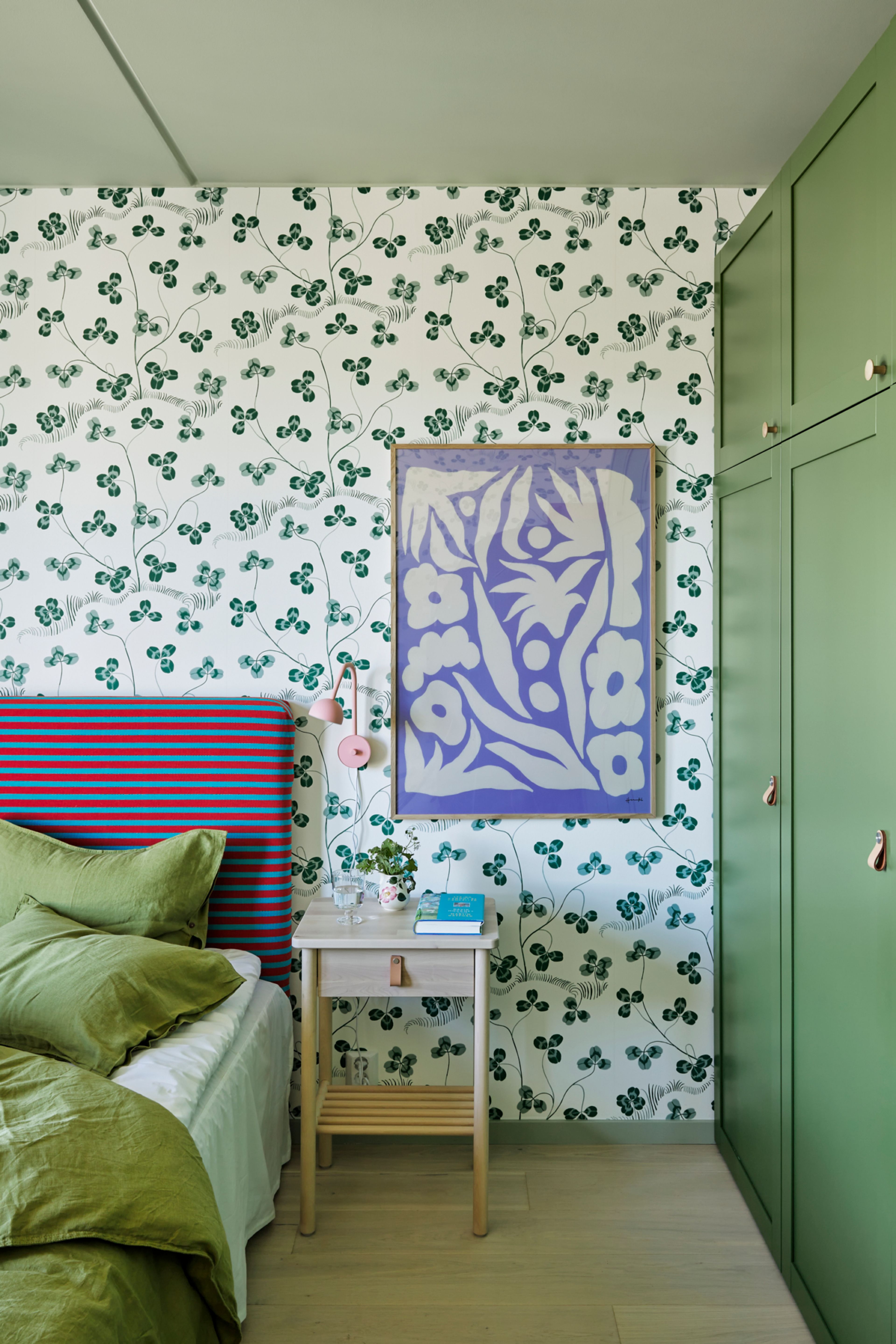 Bilde av hovedsoverommet i leiligheten med deler av sengen, sengegavl, tapet, nattbord og garderobeskap.