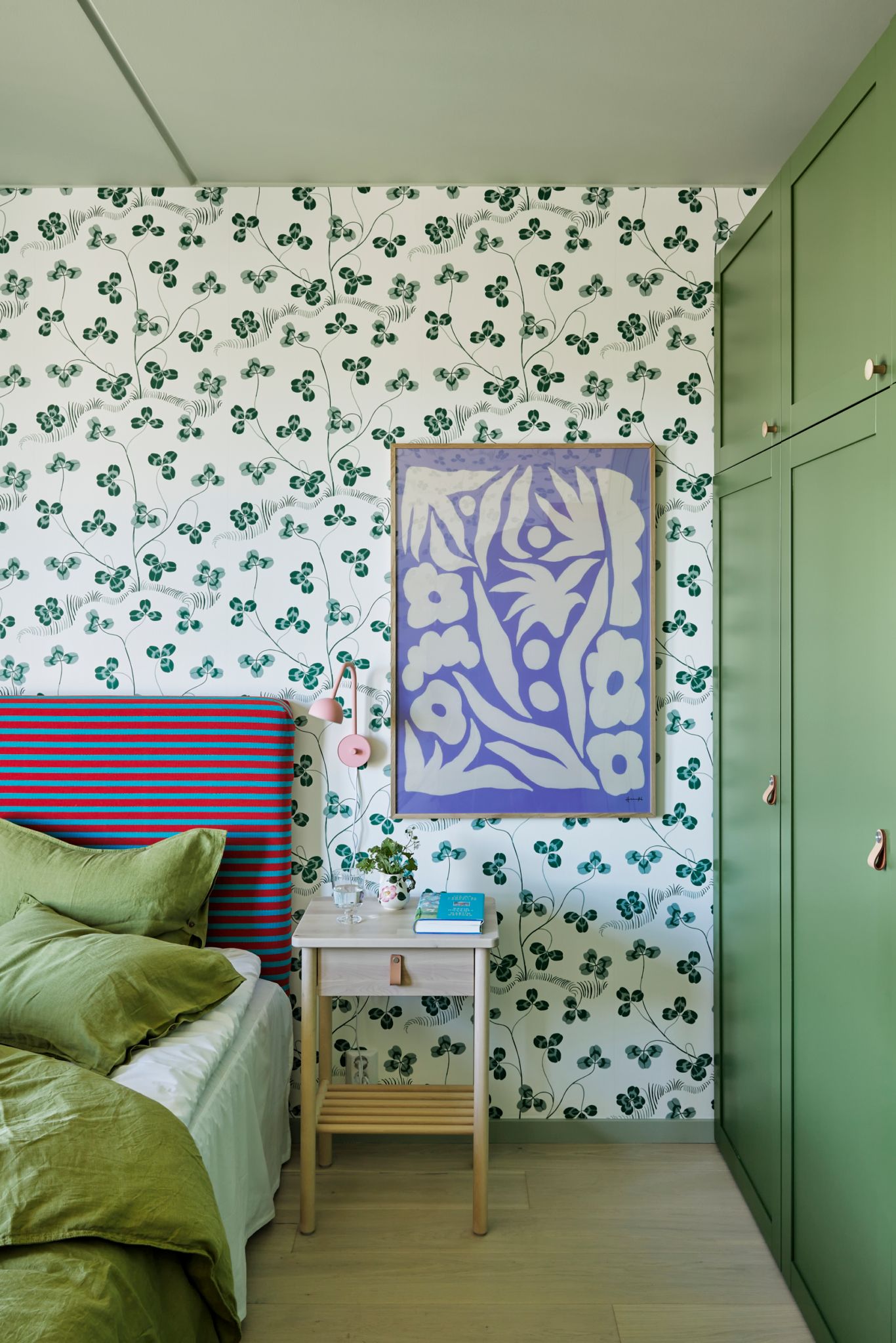 Bilde av hovedsoverommet i leiligheten med deler av sengen, sengegavl, tapet, nattbord og garderobeskap.