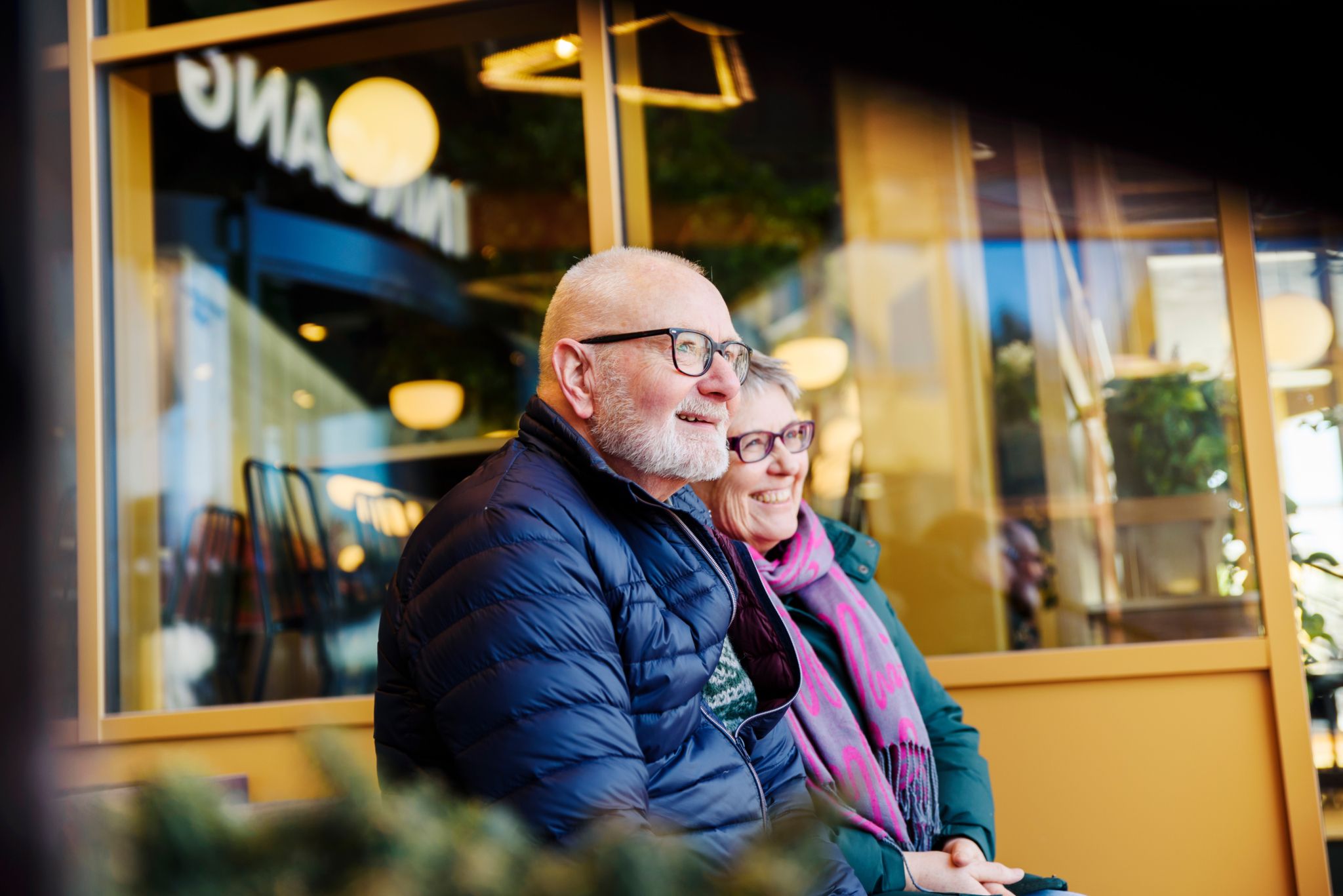 Et ektepar sitter ved siden av hverandre og har på seg boblejakker.