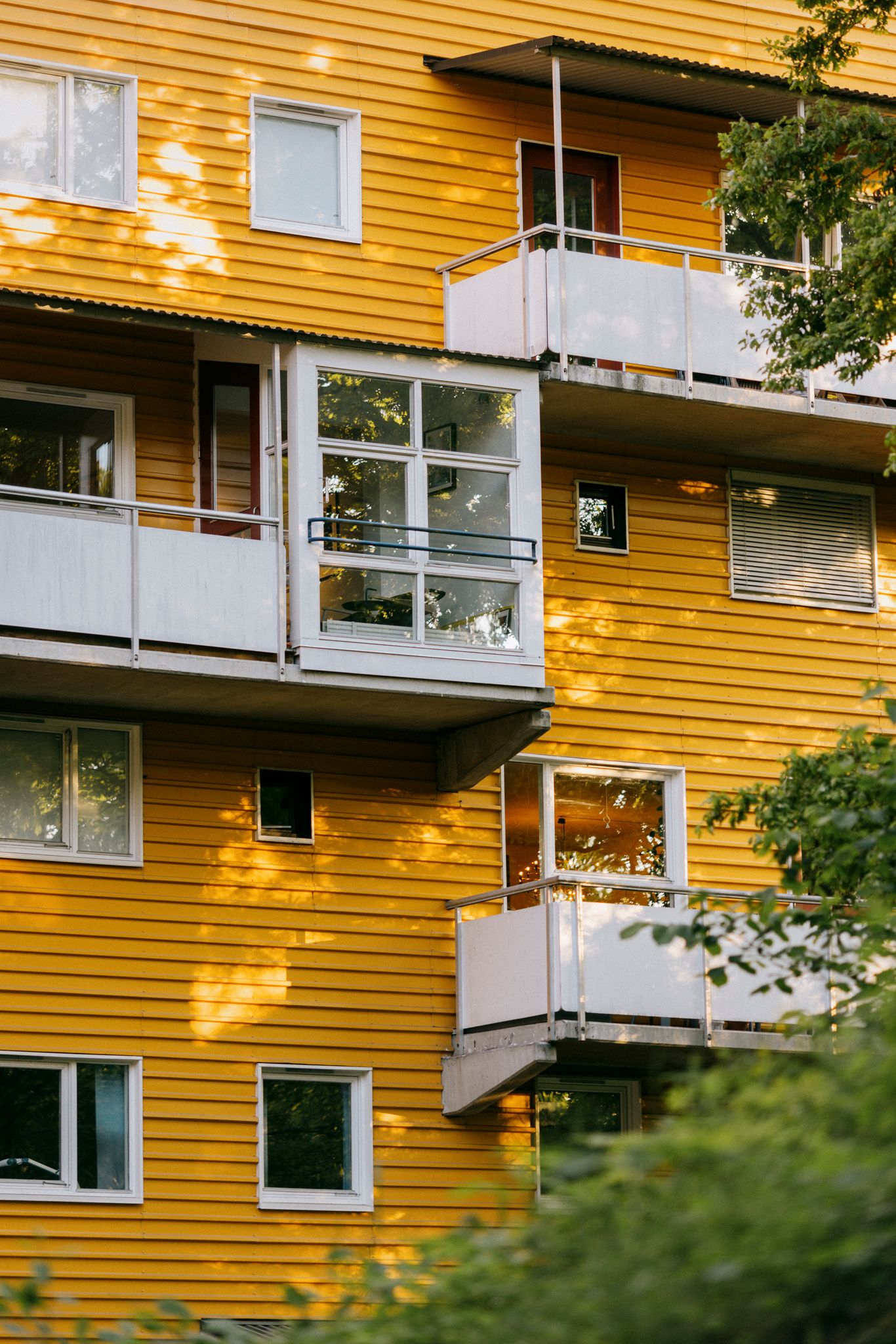 Gult bygg med hvite balkonger i Casinetto borettslag og trær i forgrunnen.