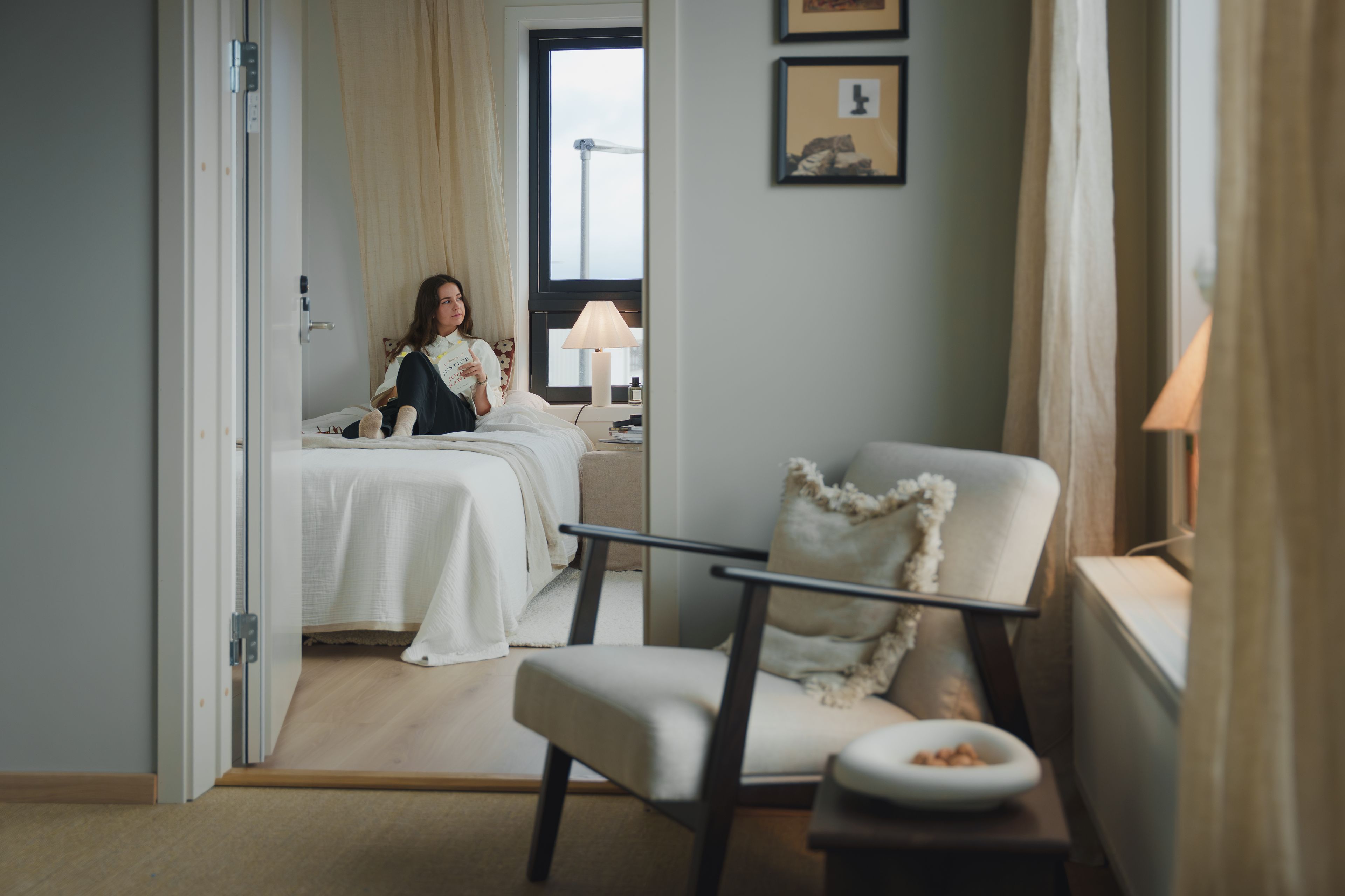 Jente sitter på soverom og leser bok. 