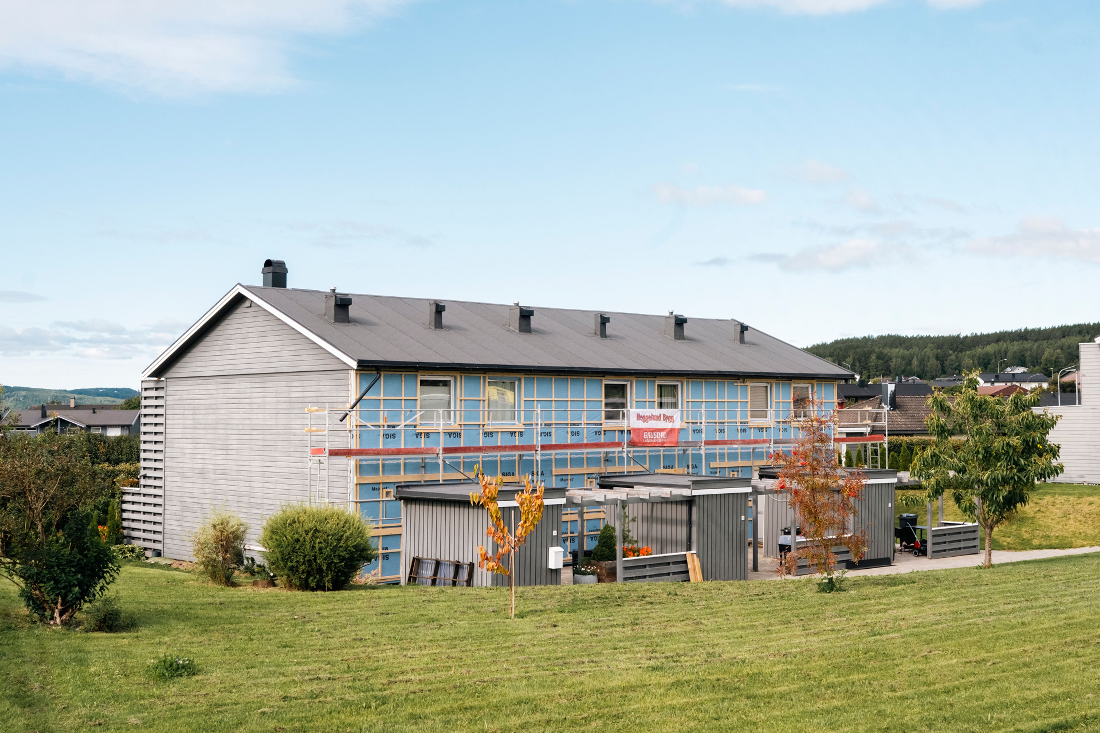 Rekkehus i Delfinen borettslag under rehabilitering, med stillas og åpen kledning på fasaden.