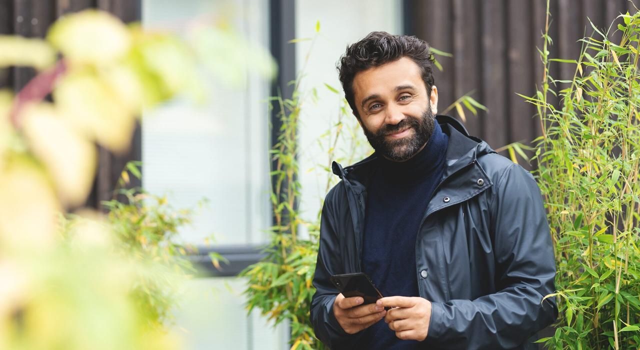 En mann står utenfor et hus og smiler mot kameraet.