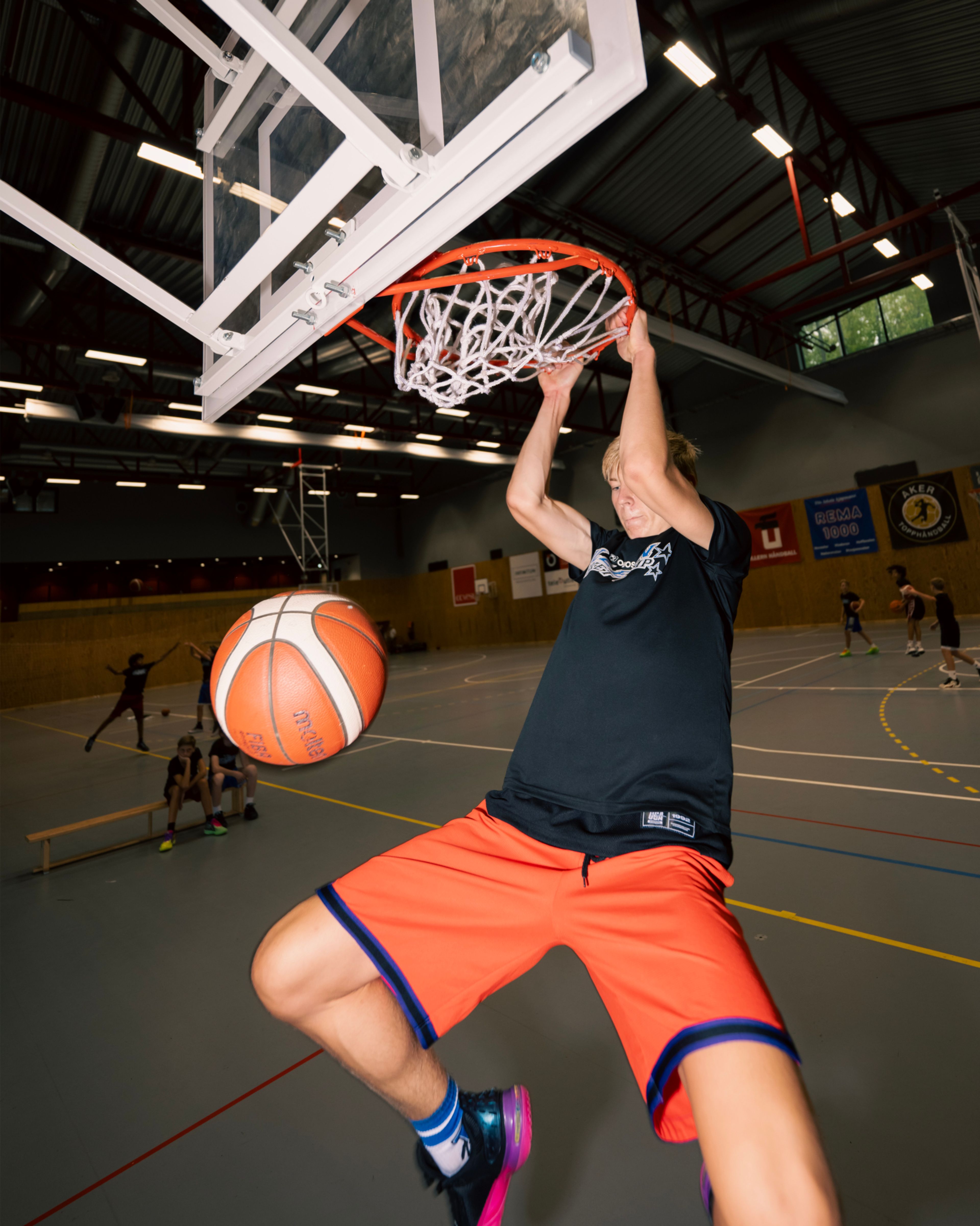 En gutt henger i basketkurven hvor basketballen akkurat har gått gjennom kurven.