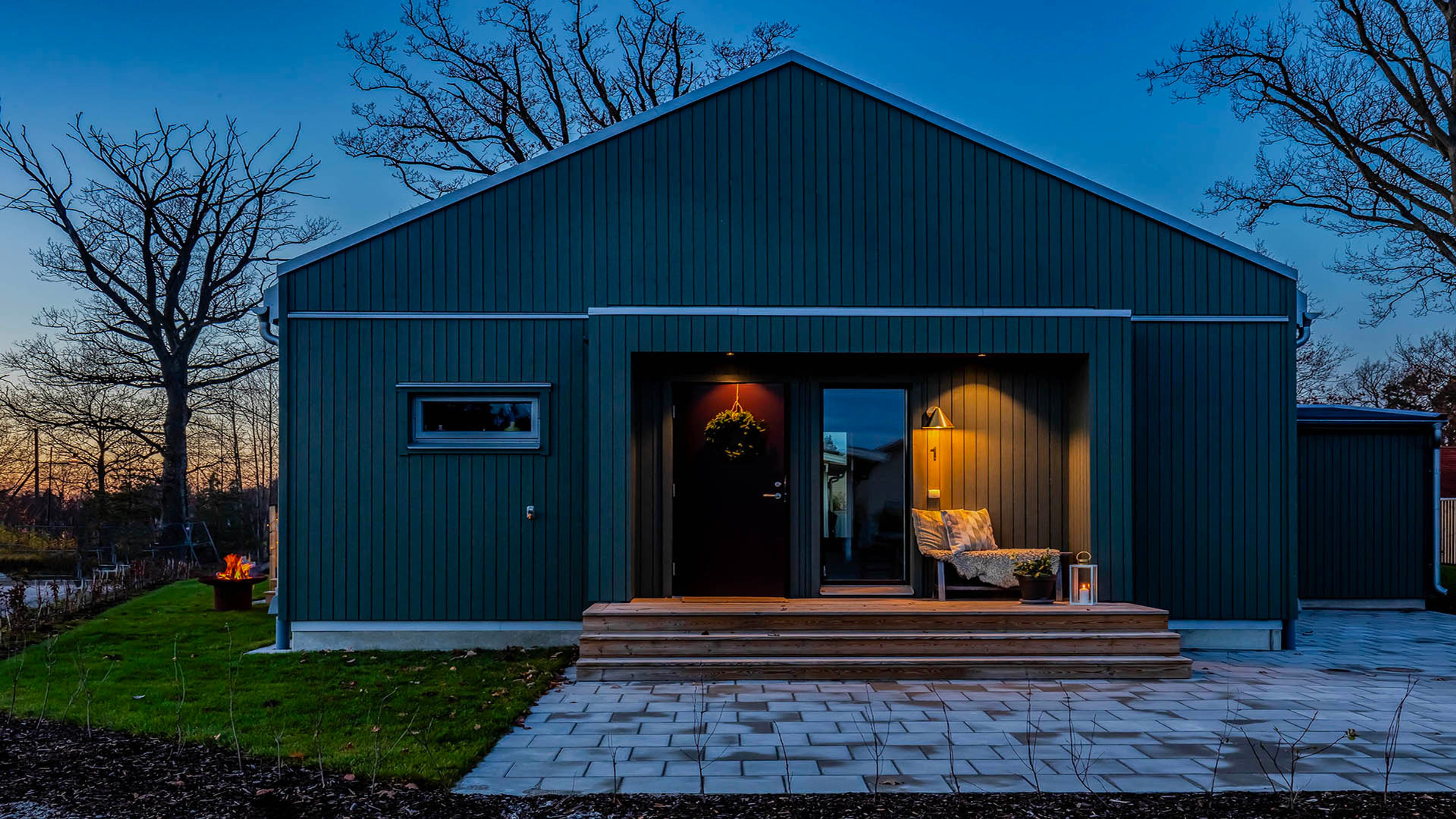 bild tagenmot entrén på ett enplanshus med svart träpanel med en trapp upp och i längst fram i bild ligger stenplattor nedanför huset.