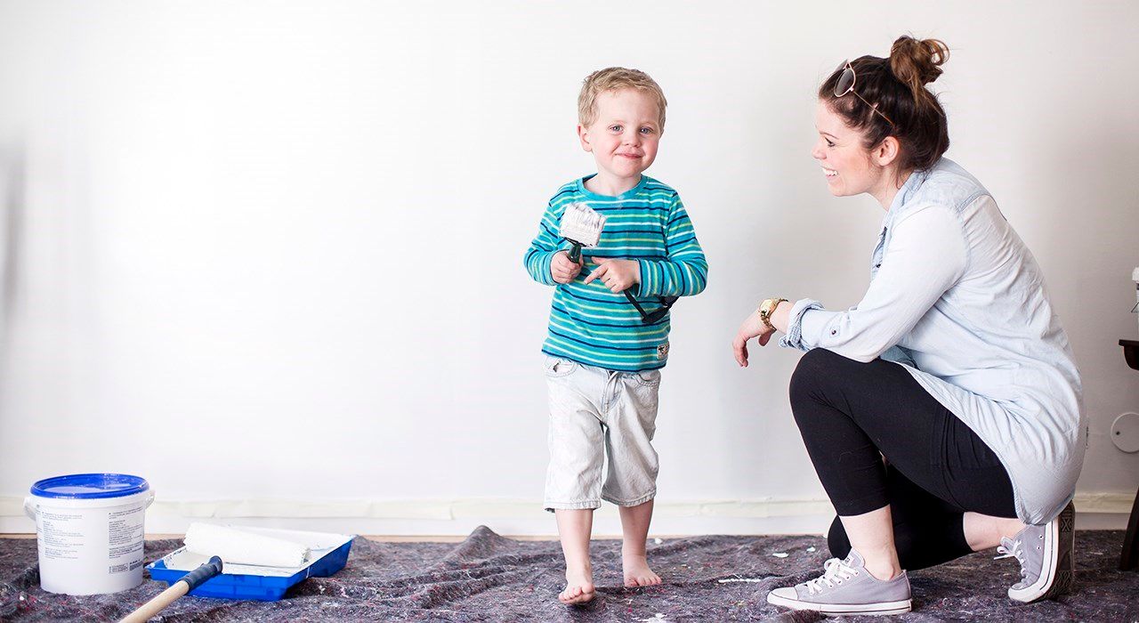 En liten gutt holder en malerpensel og moren smiler til ham.