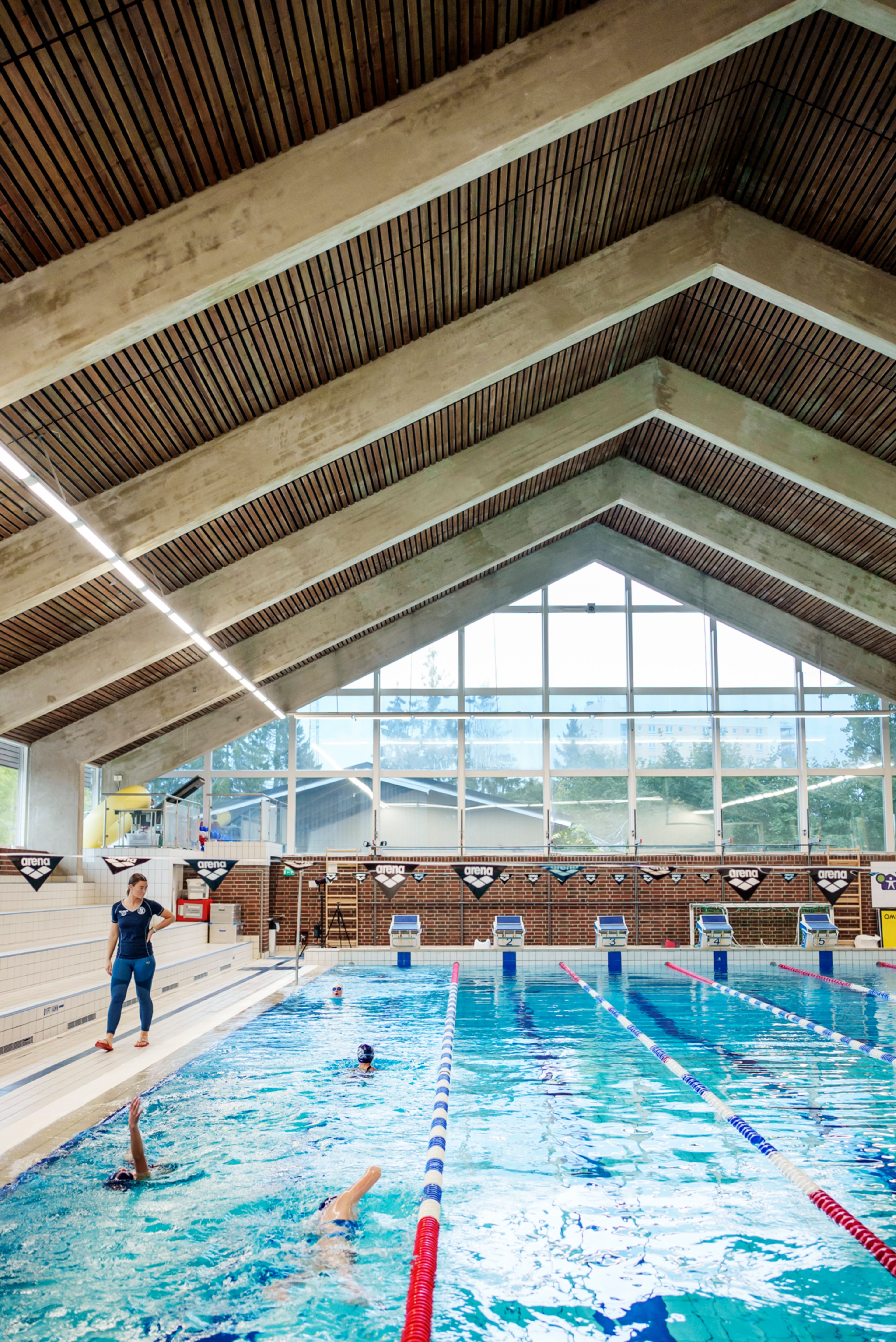 Oversiktsbilde av svømmehallen. Ei instruktør går ved siden av bassenget og følger med på barn som svømmer.