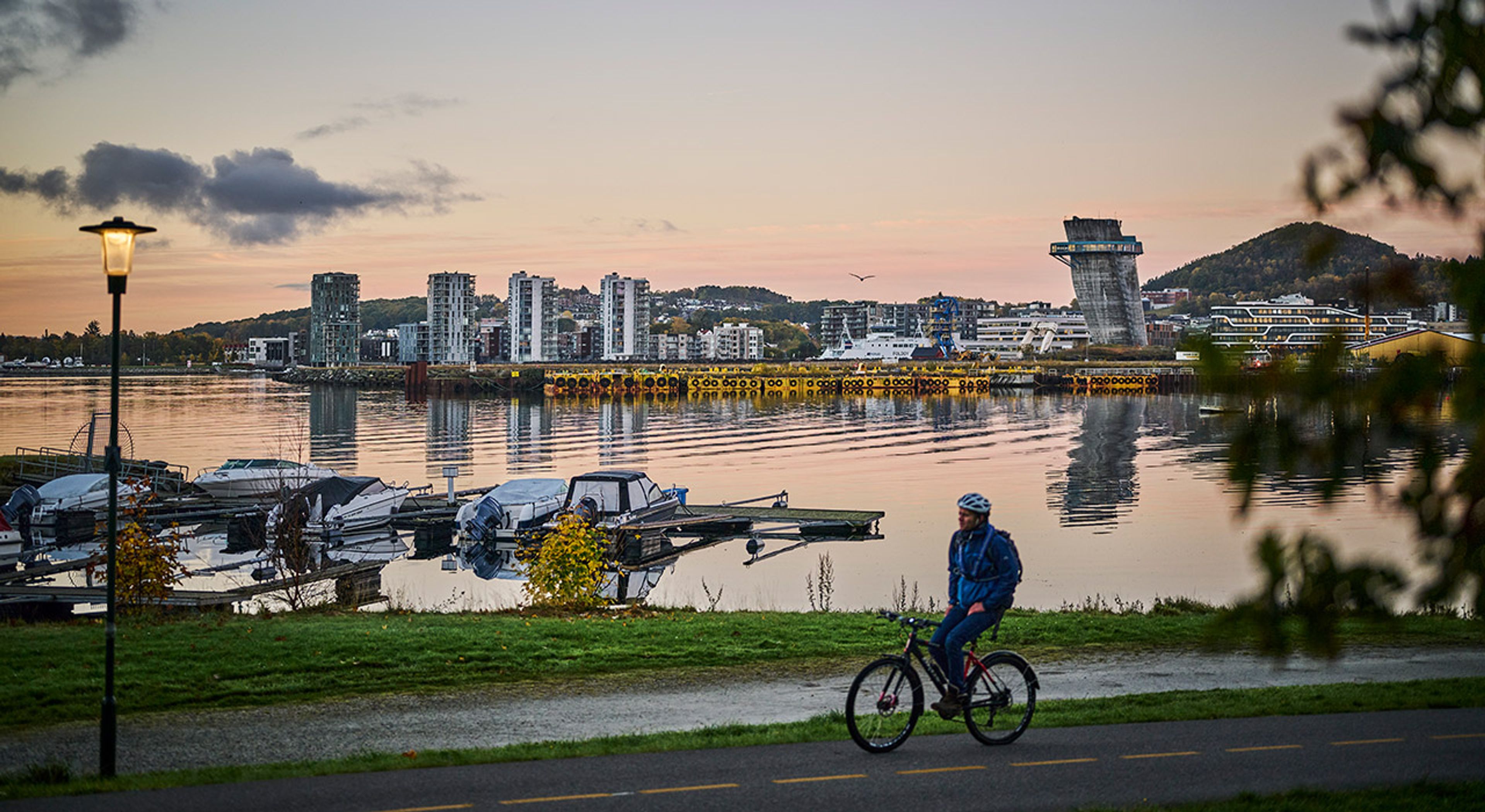 Foto av en mann som sykler ved vannet med Hinna Park i bakgrunnen.