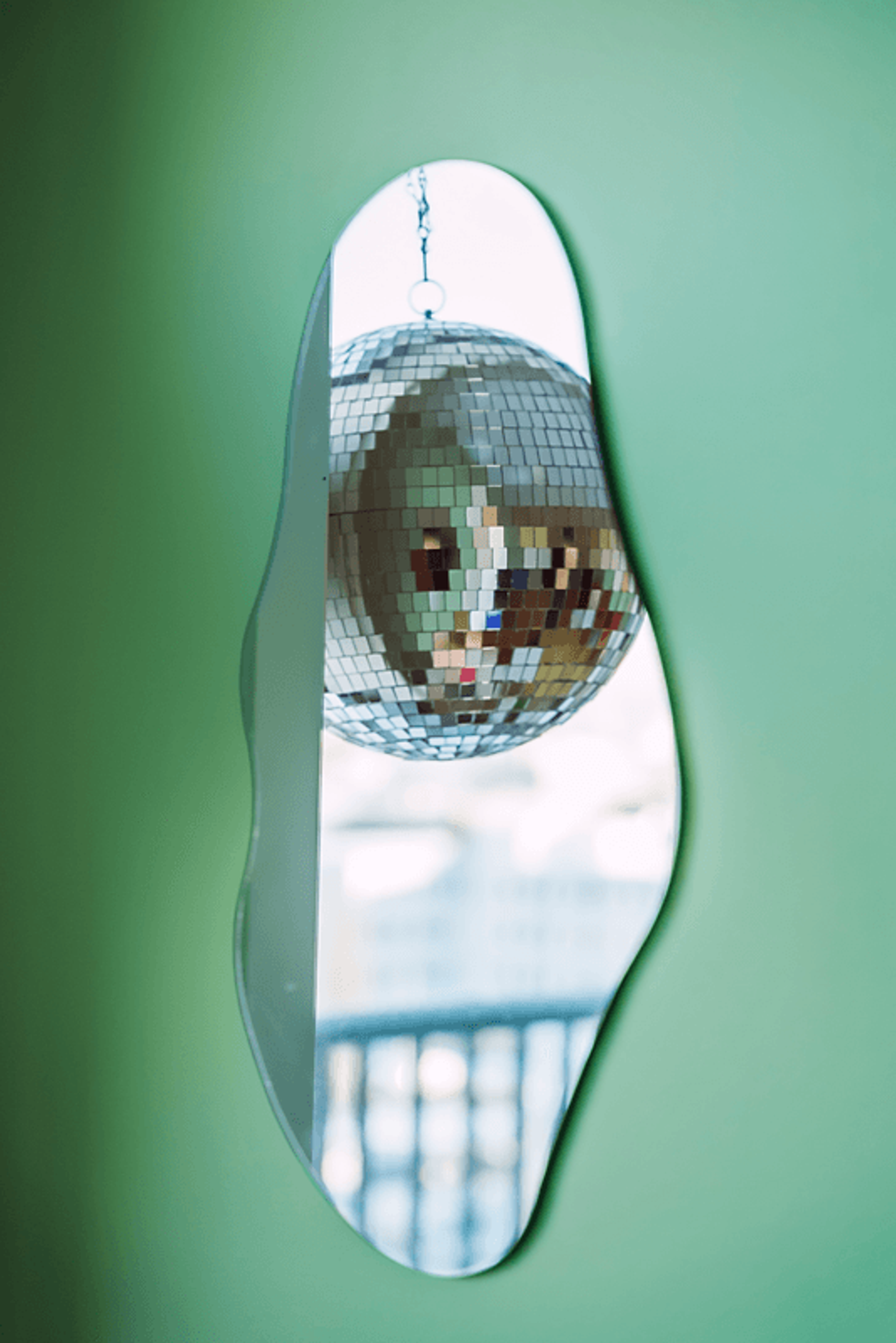 Nærbilde av et speil på stueveggen som viser en discokule hengende i vinduet fra speilbildet