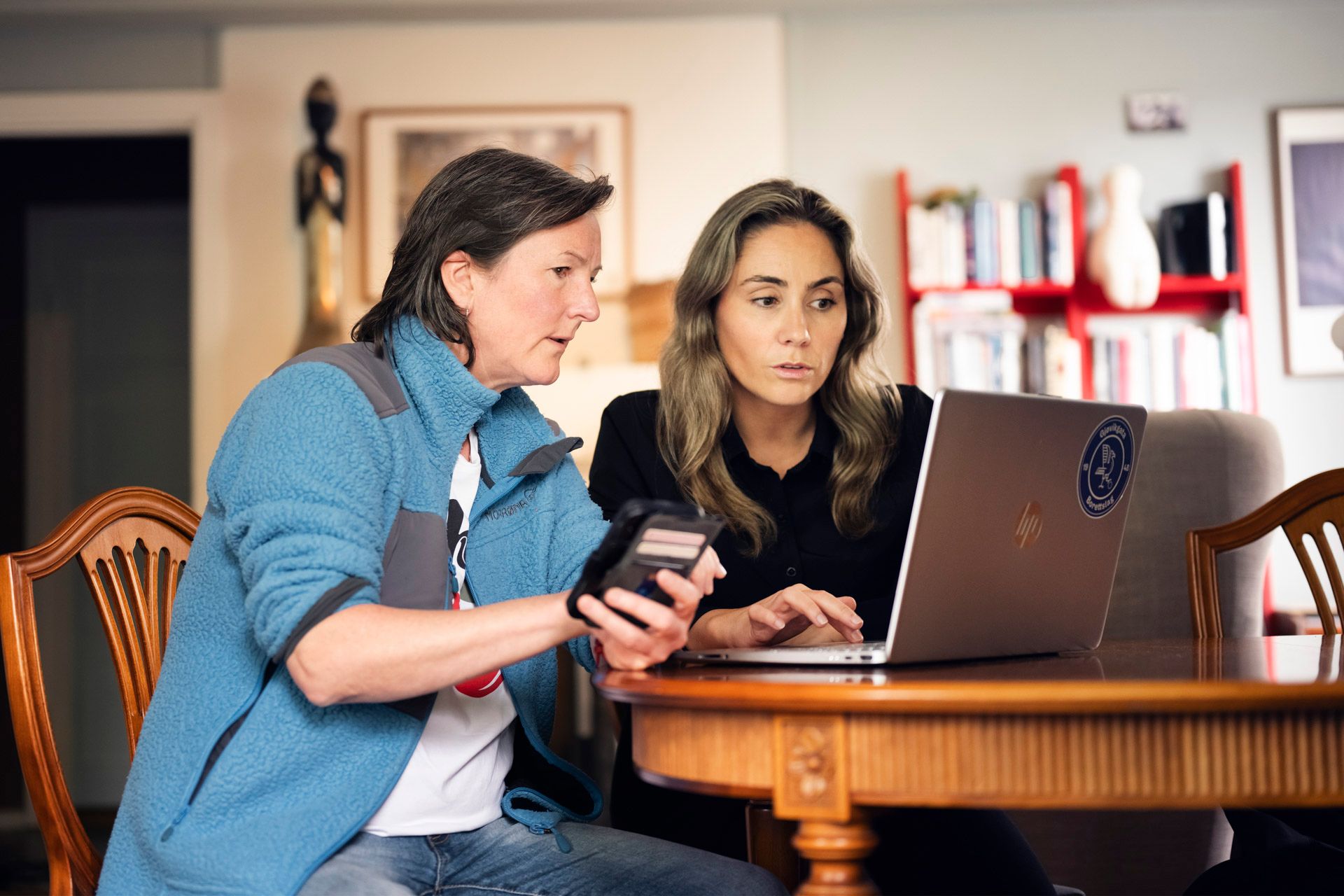To kvinner sitter foran en PC-skjerm og ser på Styrerommet sammen. Hun ene har en mobil i hånda i tillegg.