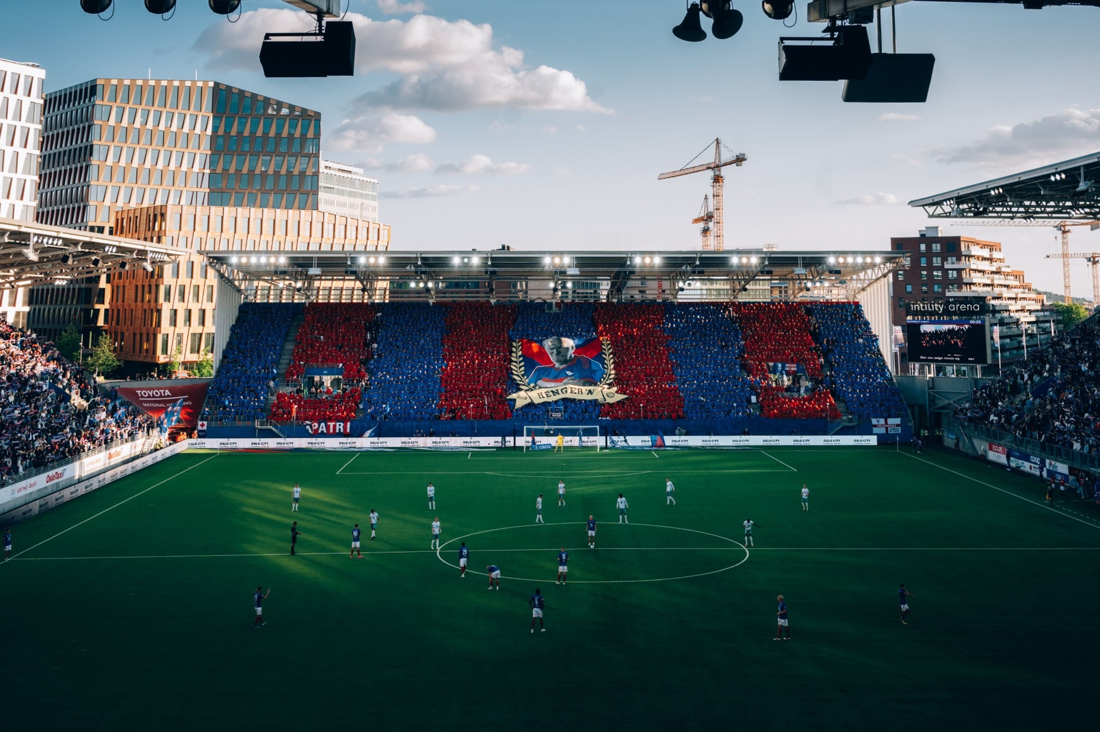 Fotballspillere fra Vålerenga etter kampslutt på Intility. Fotball Elite hilser på publikum. Store flagg i rødt, hvitt og blått vaier på tribunen.