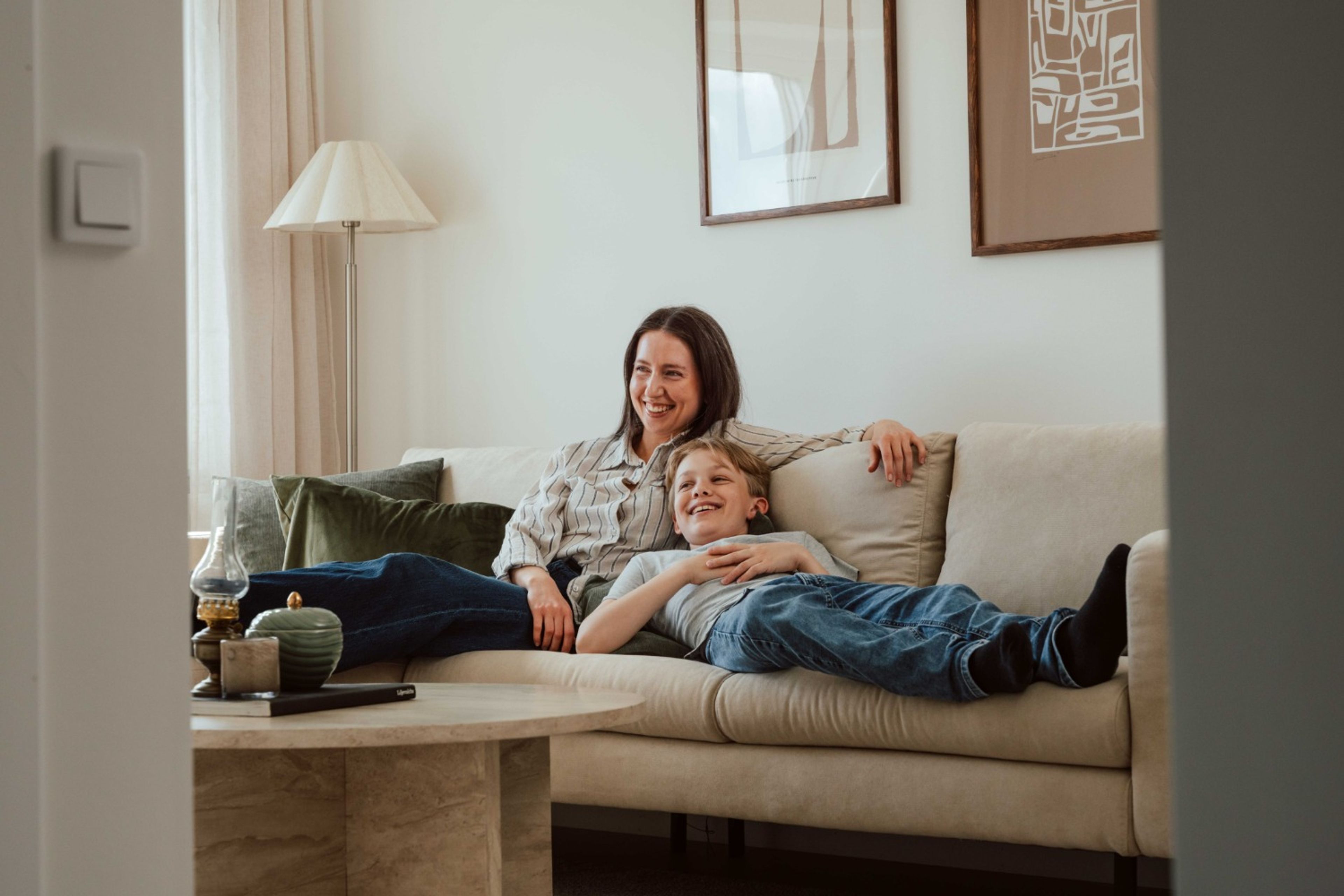 Mamma och son skrattar i en soffa, medan de tittar på TV