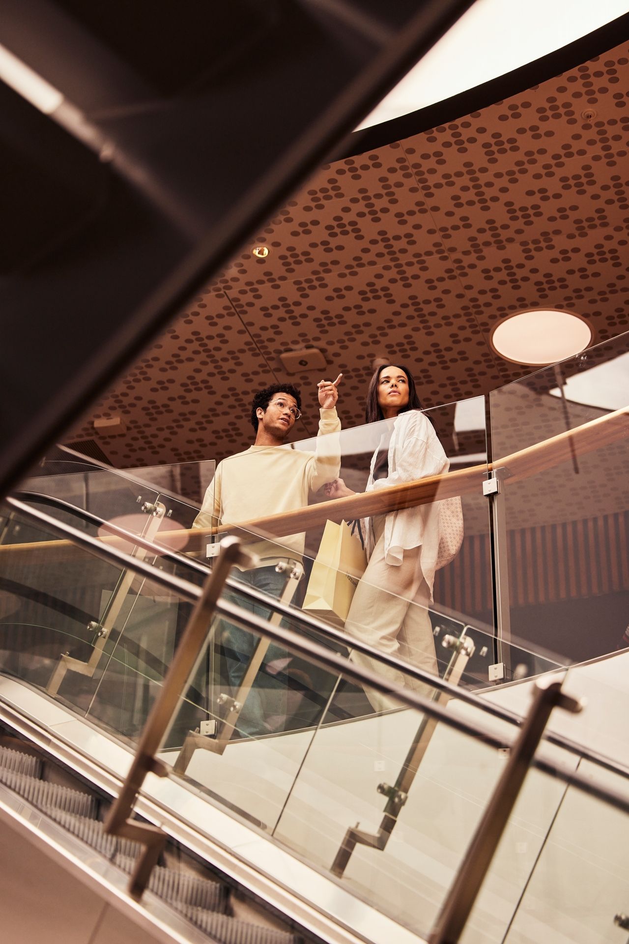 Dame og mann som står og ser ned ved en rulletrapp på senteret Fornebu S