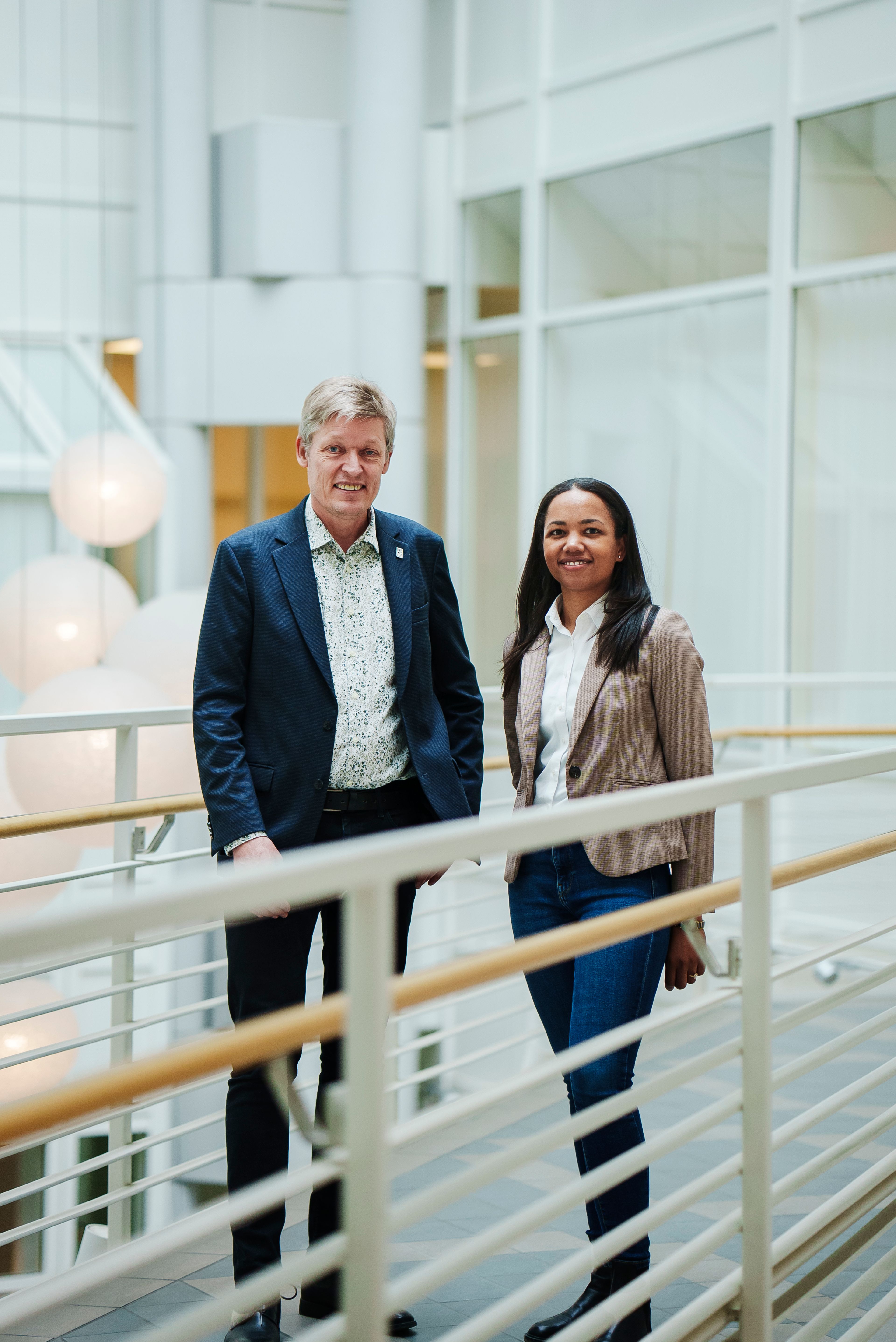 En mann og en kvinne står inntil hverandre og smiler på en bro inne i Høyskolen Kristiania sitt campus.