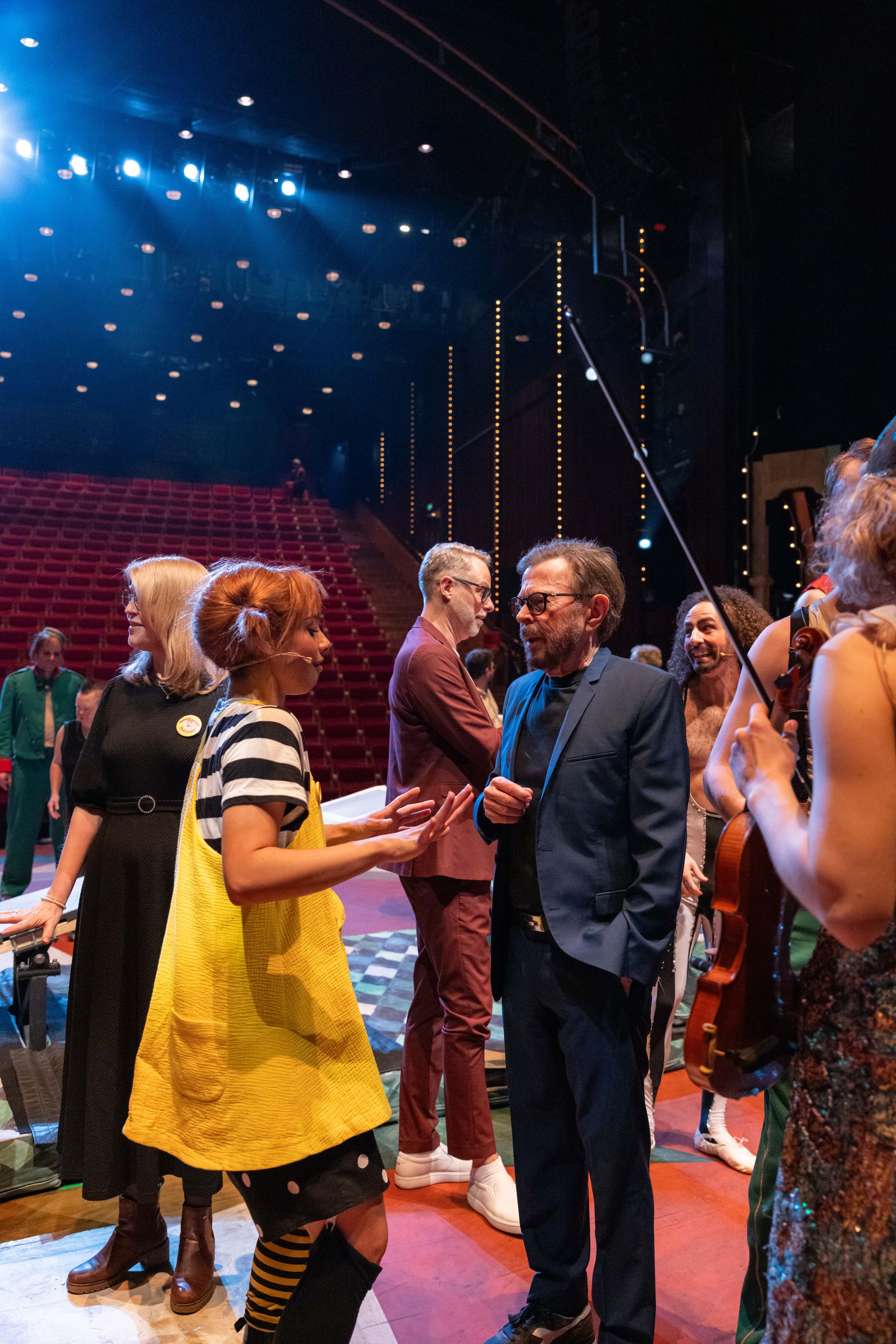 Ulvaeus i mørk blazer i samtale med skuespilleren i Pippi-kostyme med gul kjole og utstående fletter, på scenen.