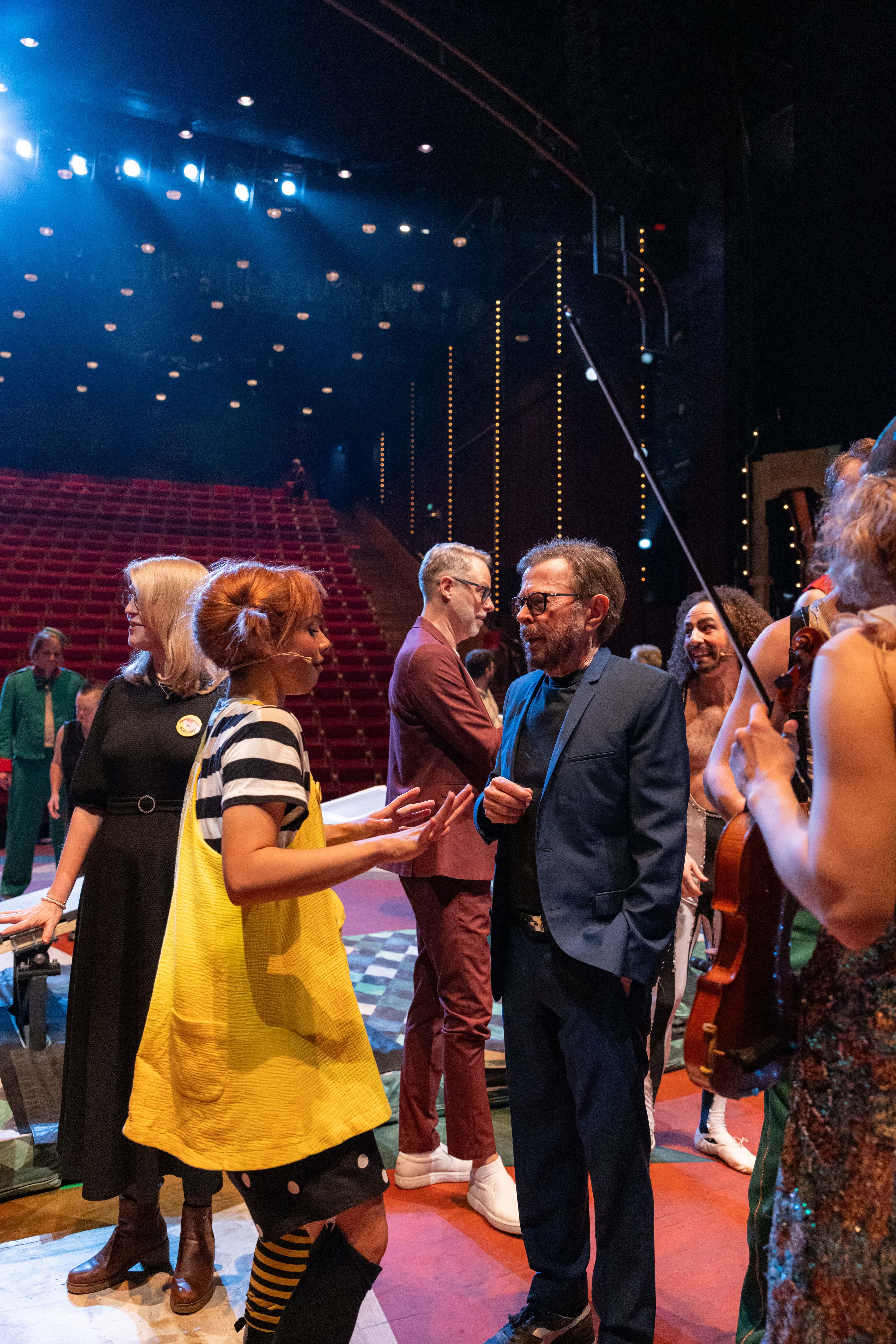 Ulvaeus i mørk blazer i samtale med skuespilleren i Pippi-kostyme med gul kjole og utstående fletter, på scenen.