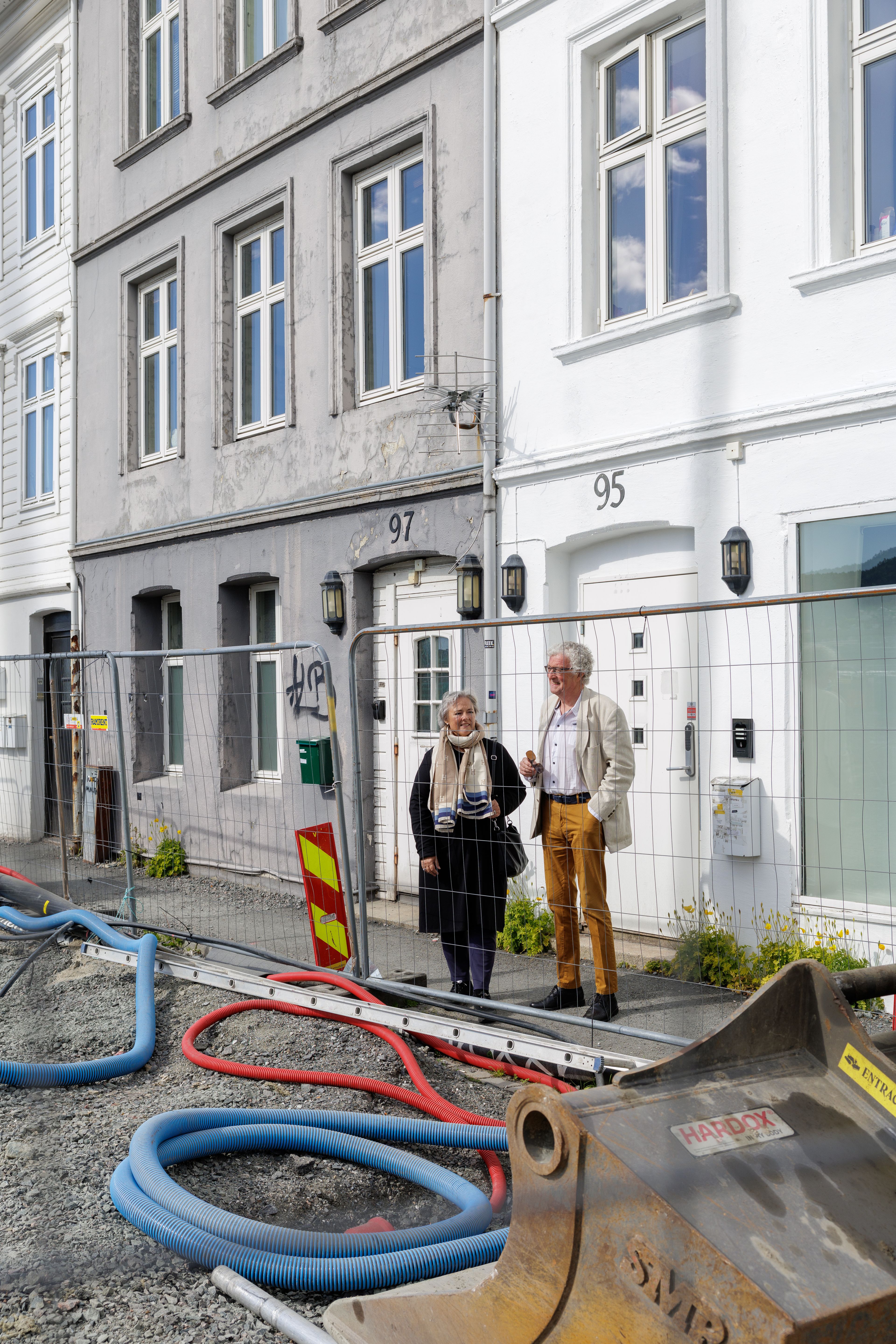 Edna og Øyvind står og diskuterer bak gjerdet til byggeplassen for Nøstebukten Brygge