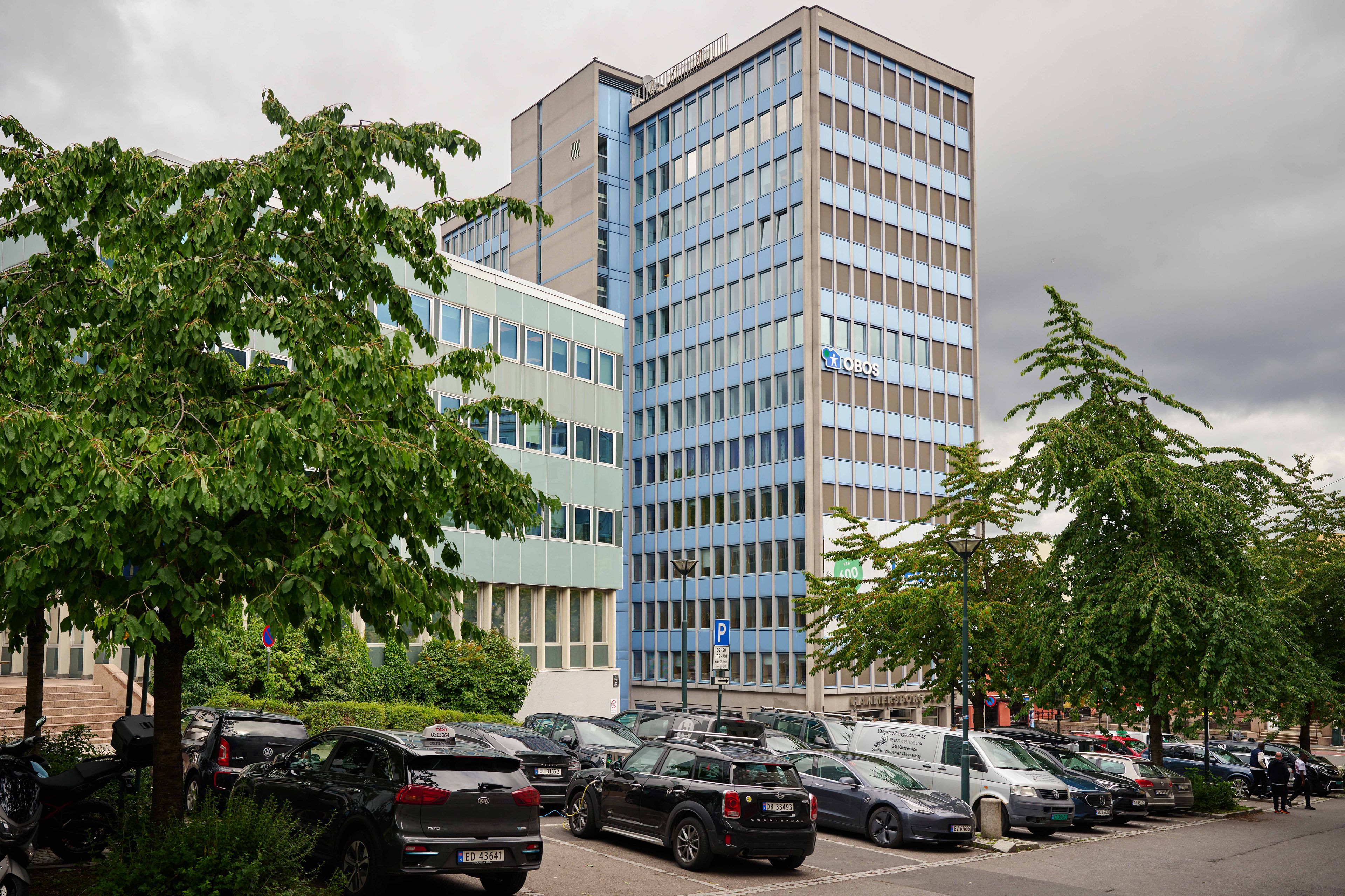 Foto av Hammersborg Torg tatt fra parkeringsplassen foran byggene.