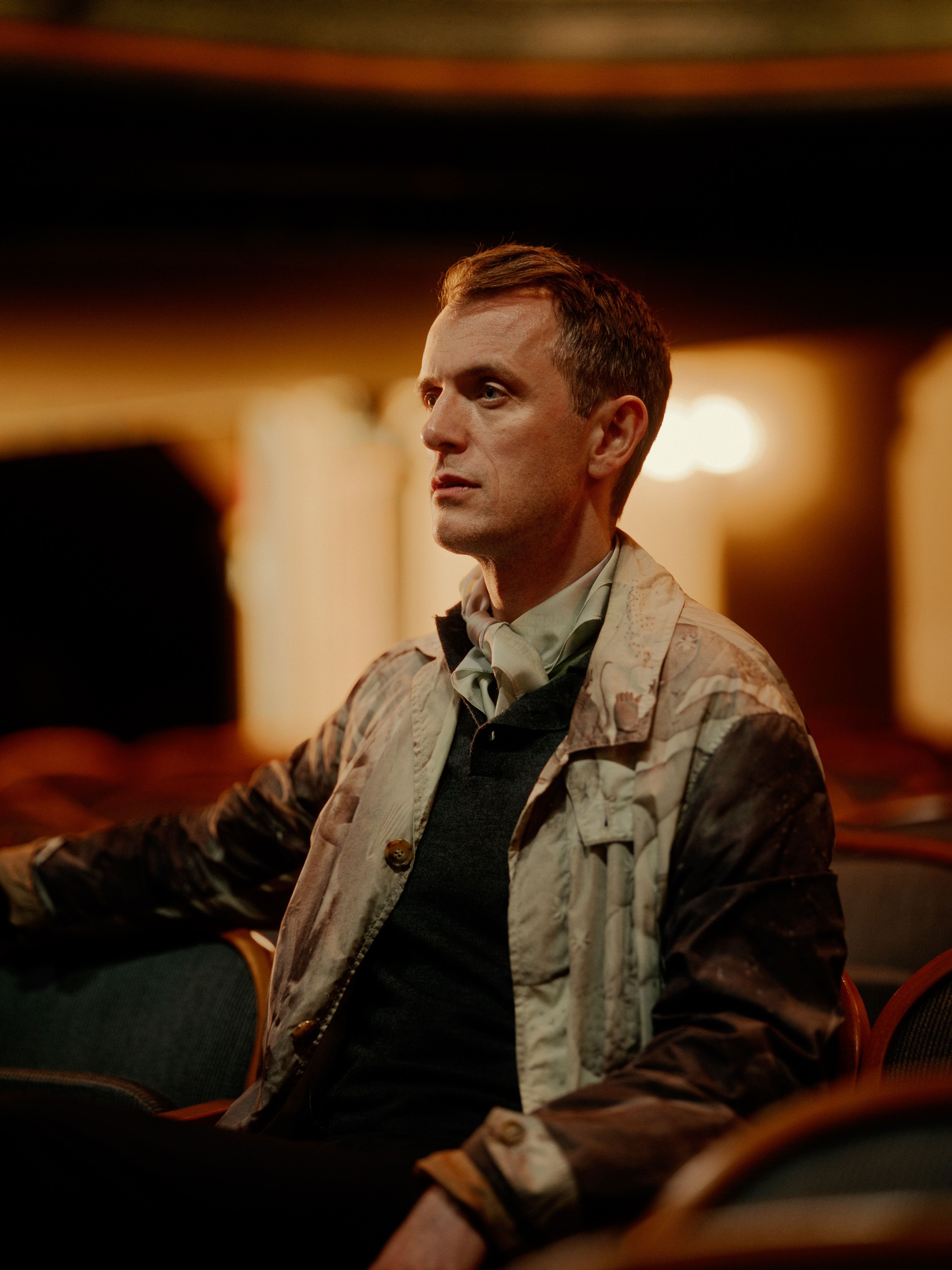 Nils Bech sitter dunkelt belyst i salen på Centralteatret, halvveis i profil med venstre side av ansiktet mot kamera