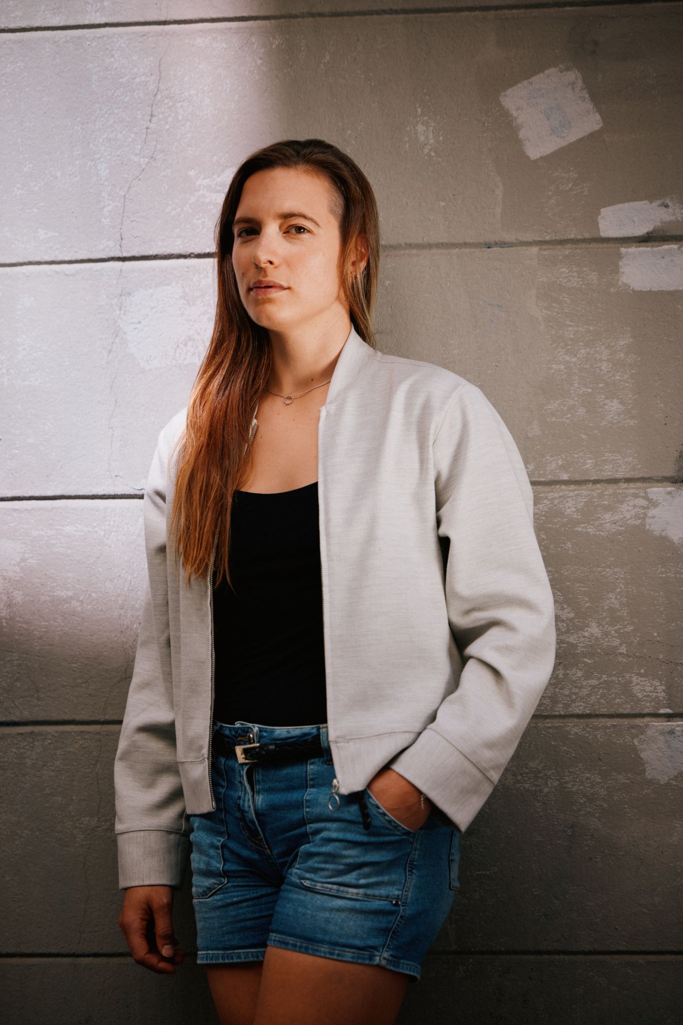 Inga Strumke står inntil en vegg. Hun har på en grå jakke og en olashorts.