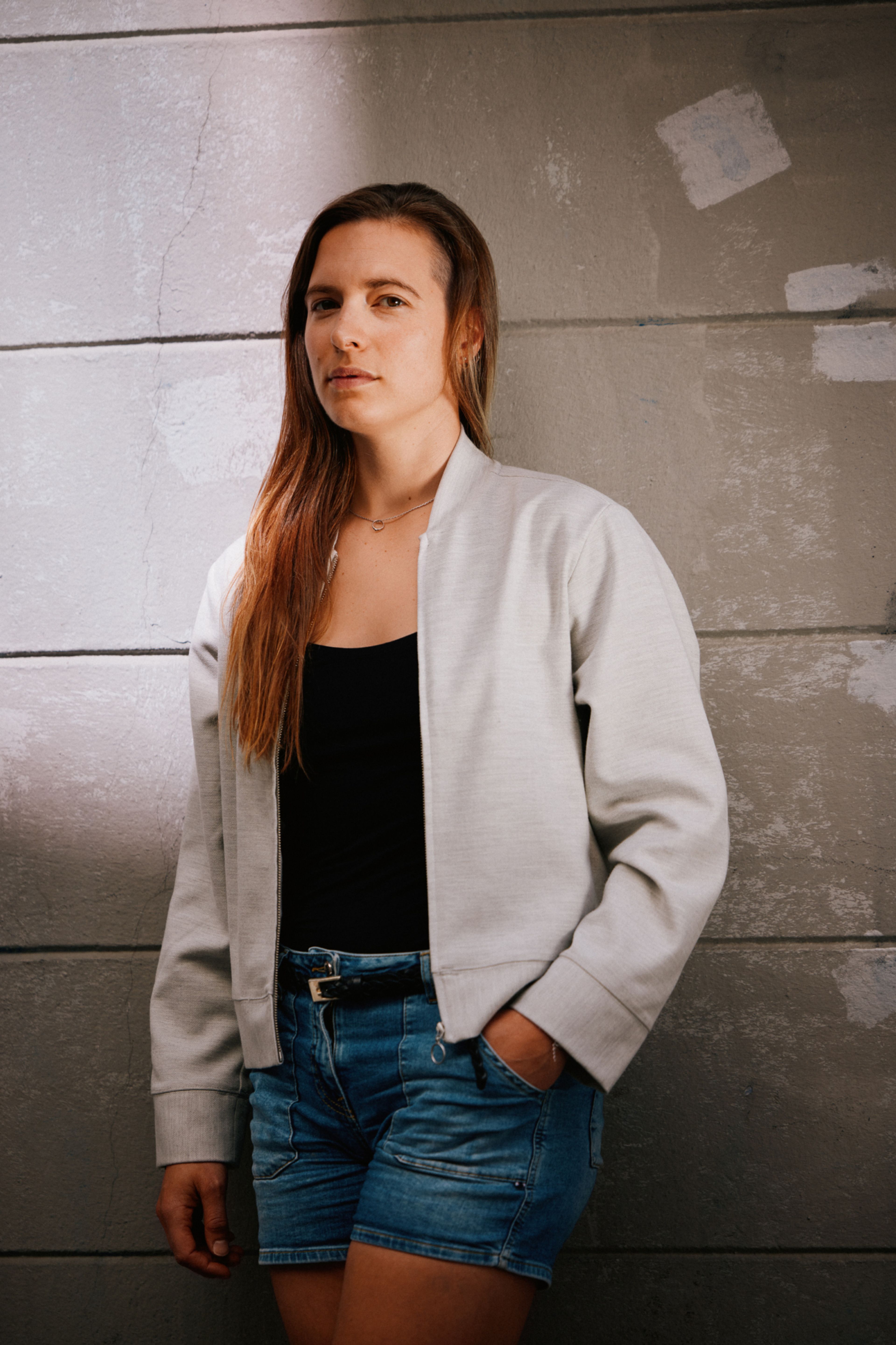 Inga Strumke står inntil en vegg. Hun har på en grå jakke og en olashorts.