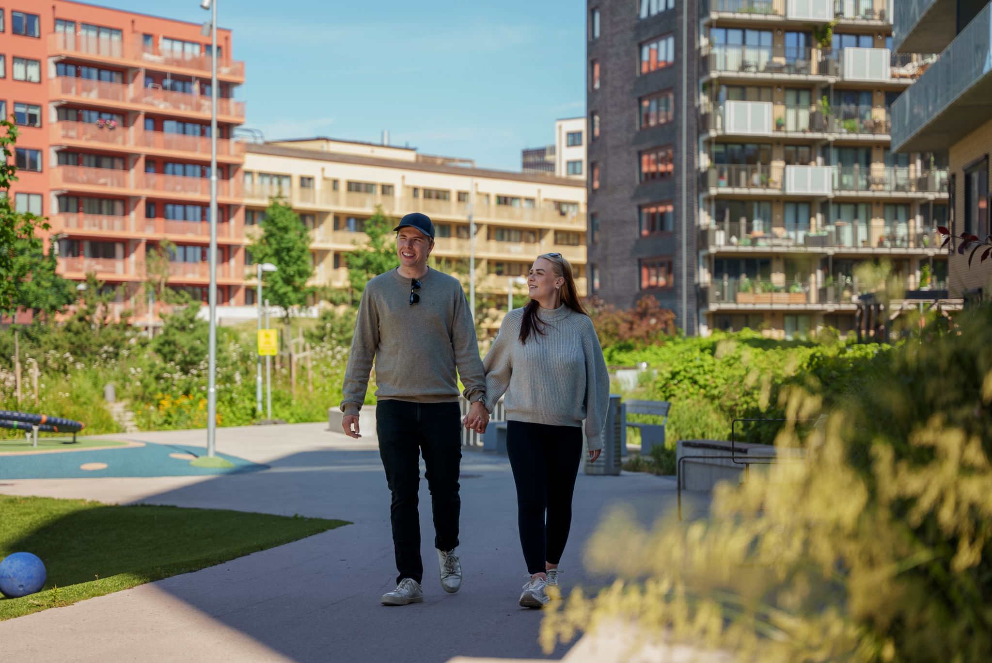 Lars Erik Jensen og Martine Nydahl Svehagen går hånd i hånd mellom boligblokker på Ulven. Sol og fint vær og grønne trær.