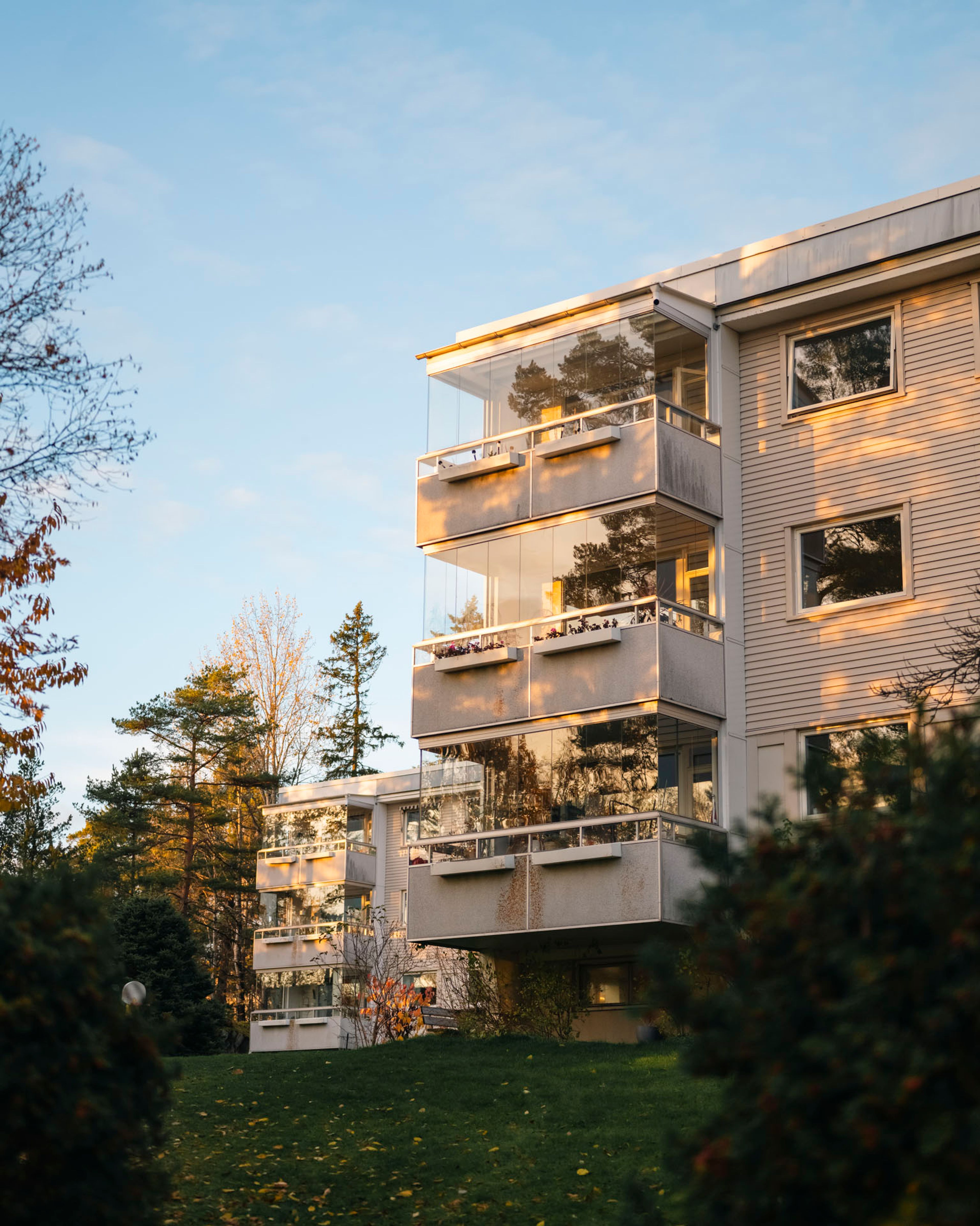 Fasade av boligblokk i Munkelia borettslag, med sollys og trær i forgrunnen.