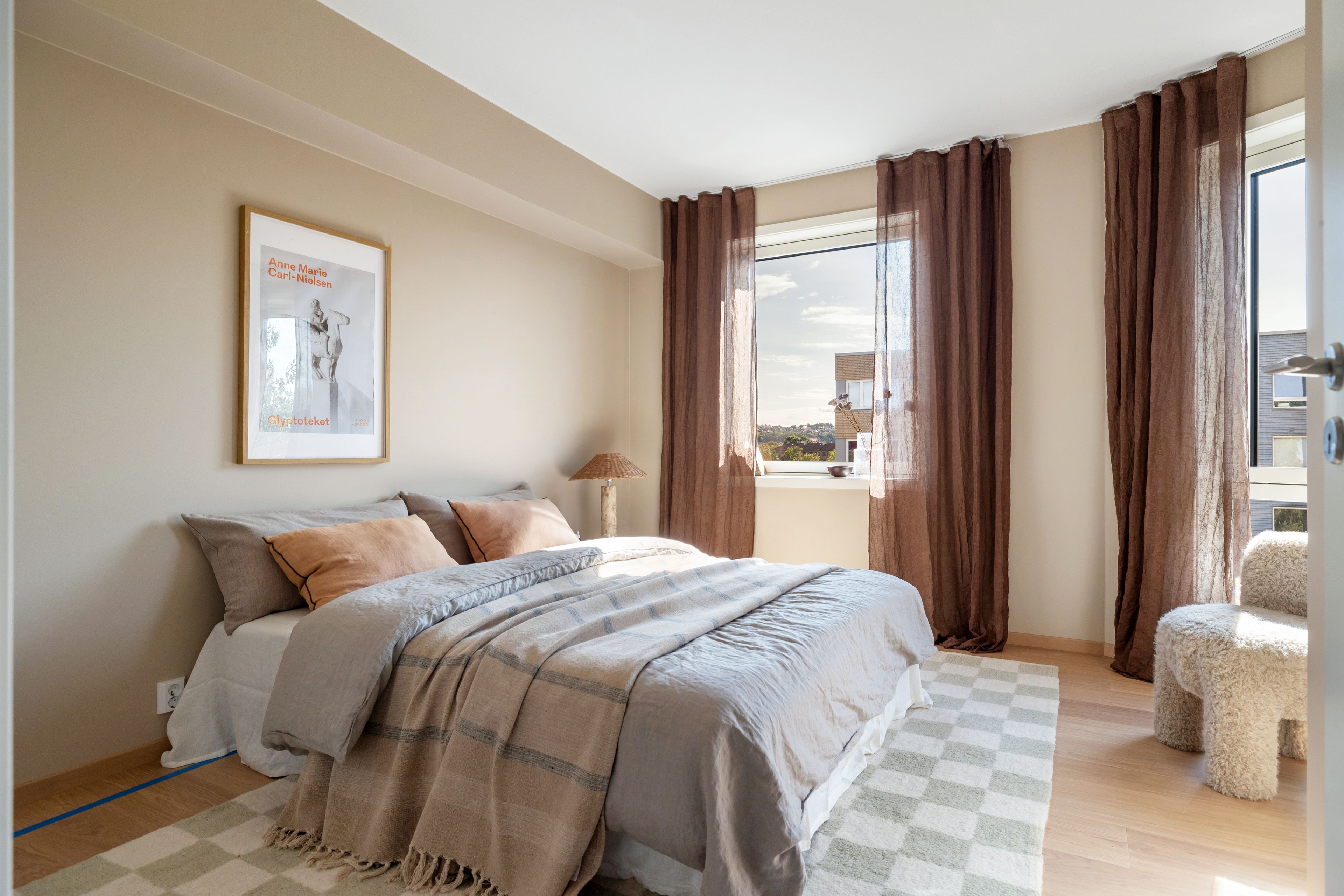 Foto av hovedsoverommet. Inntil veggen er det en stor dobbeltseng med luftige puter. Det er vinduer på flere vegger som slipper inn rikelig med naturlig lys.