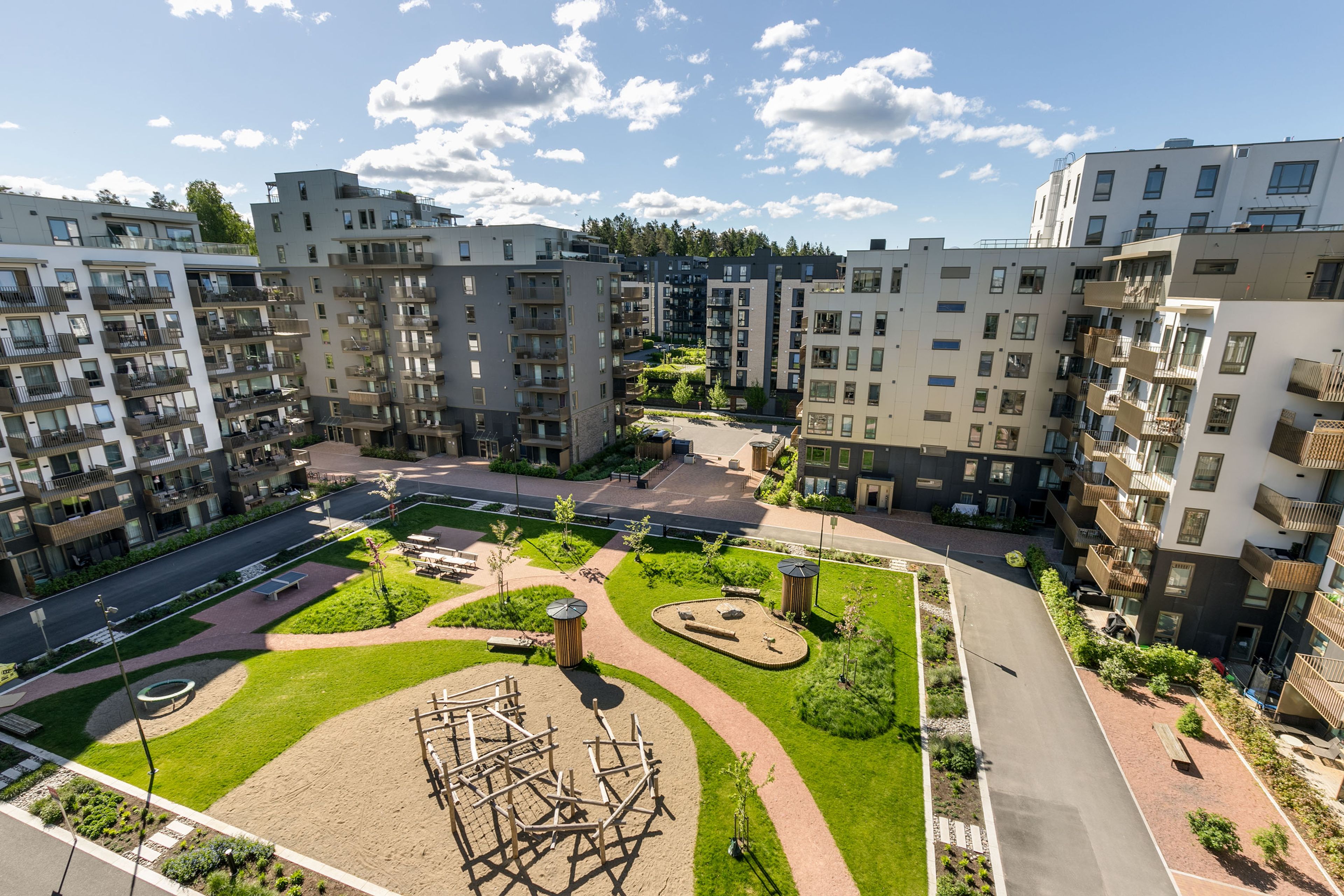 Oversiktsbilde over frodig fellesområde med park og lekestativer mellom husene på MIDT