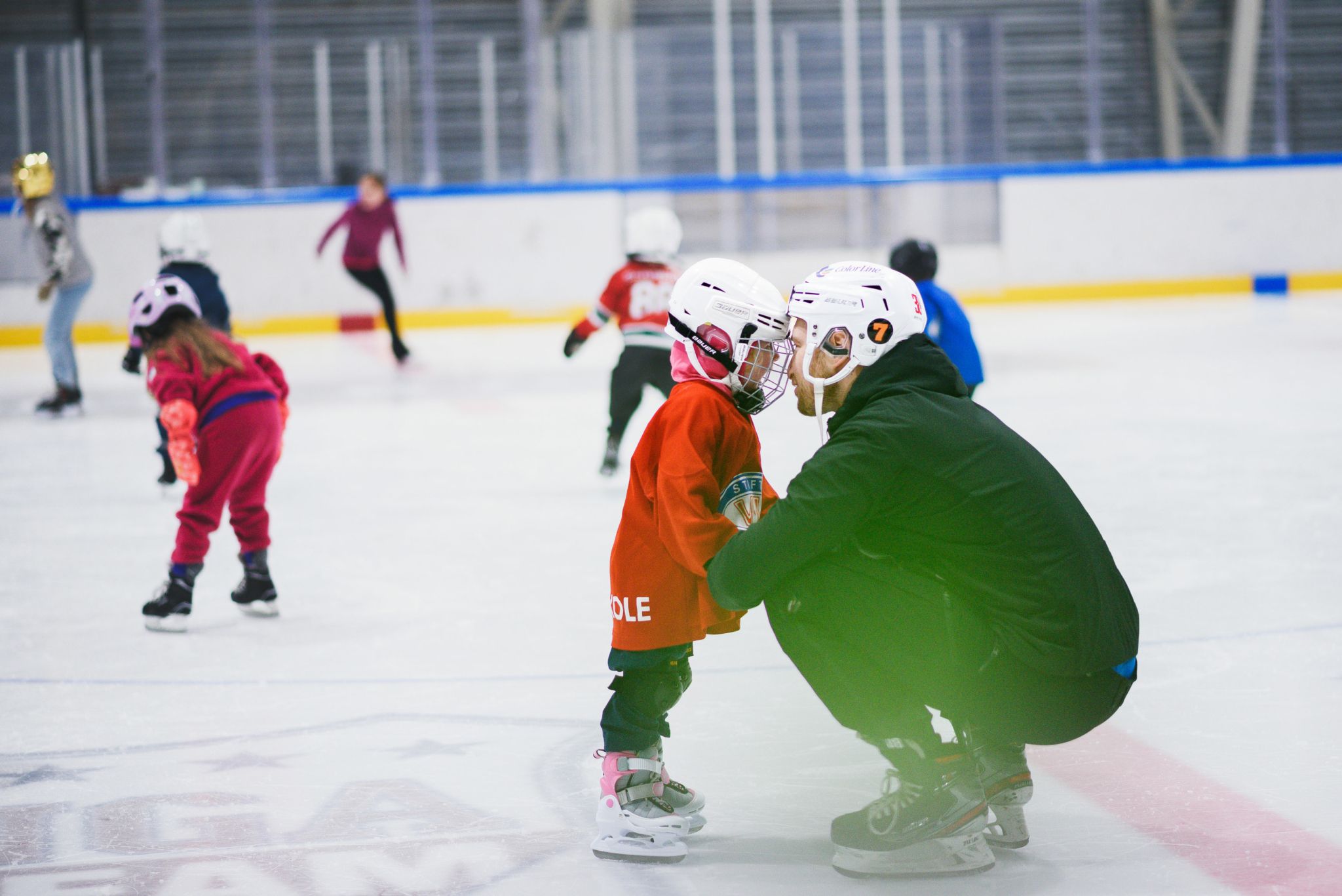 Foto av et barn med hockeyutstyr står på isen mens han lener ansiktet inn mot skøytetreneren og ser han inn i øynene.