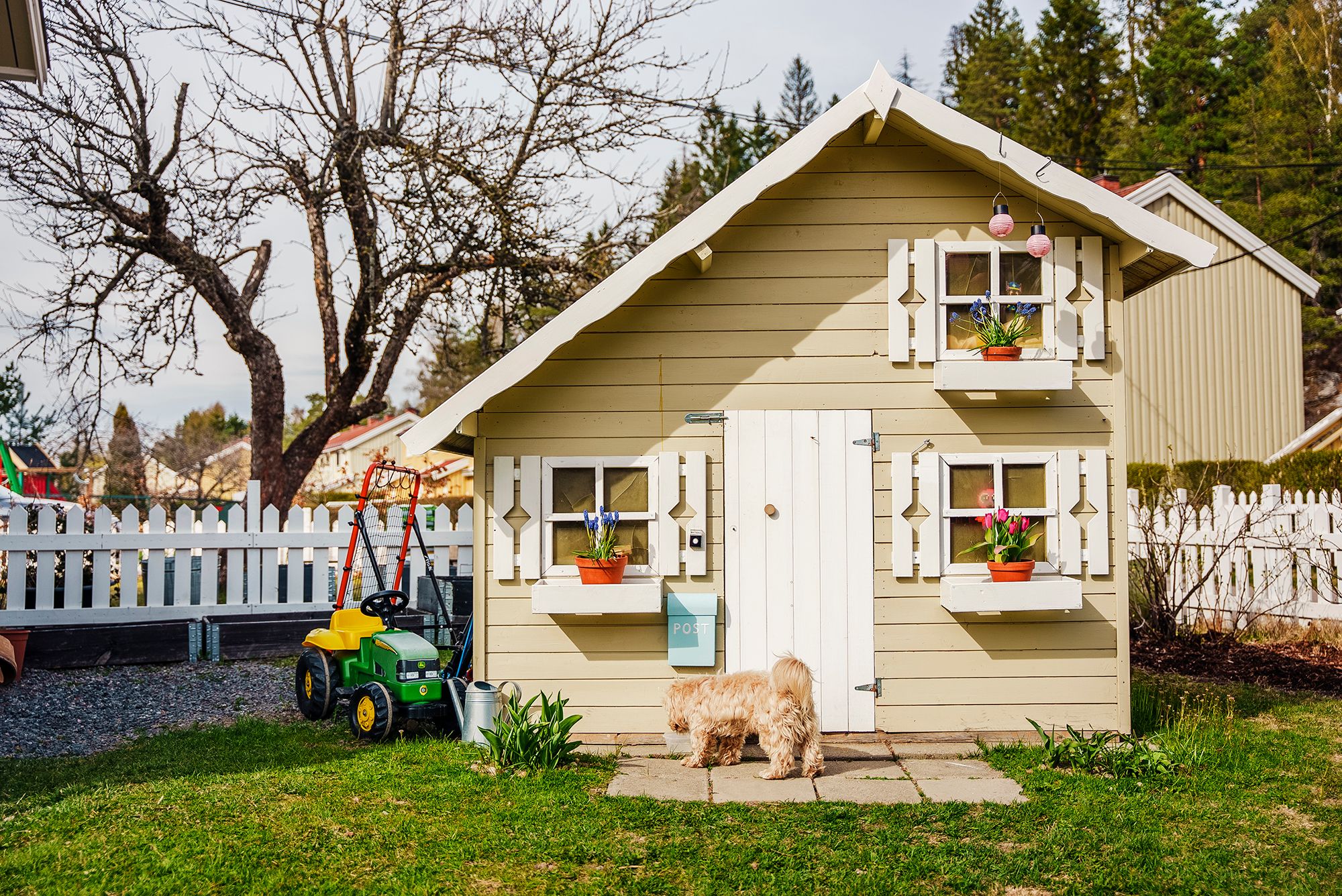 Gult lekehus i hagen med en liten hund foran døren.
