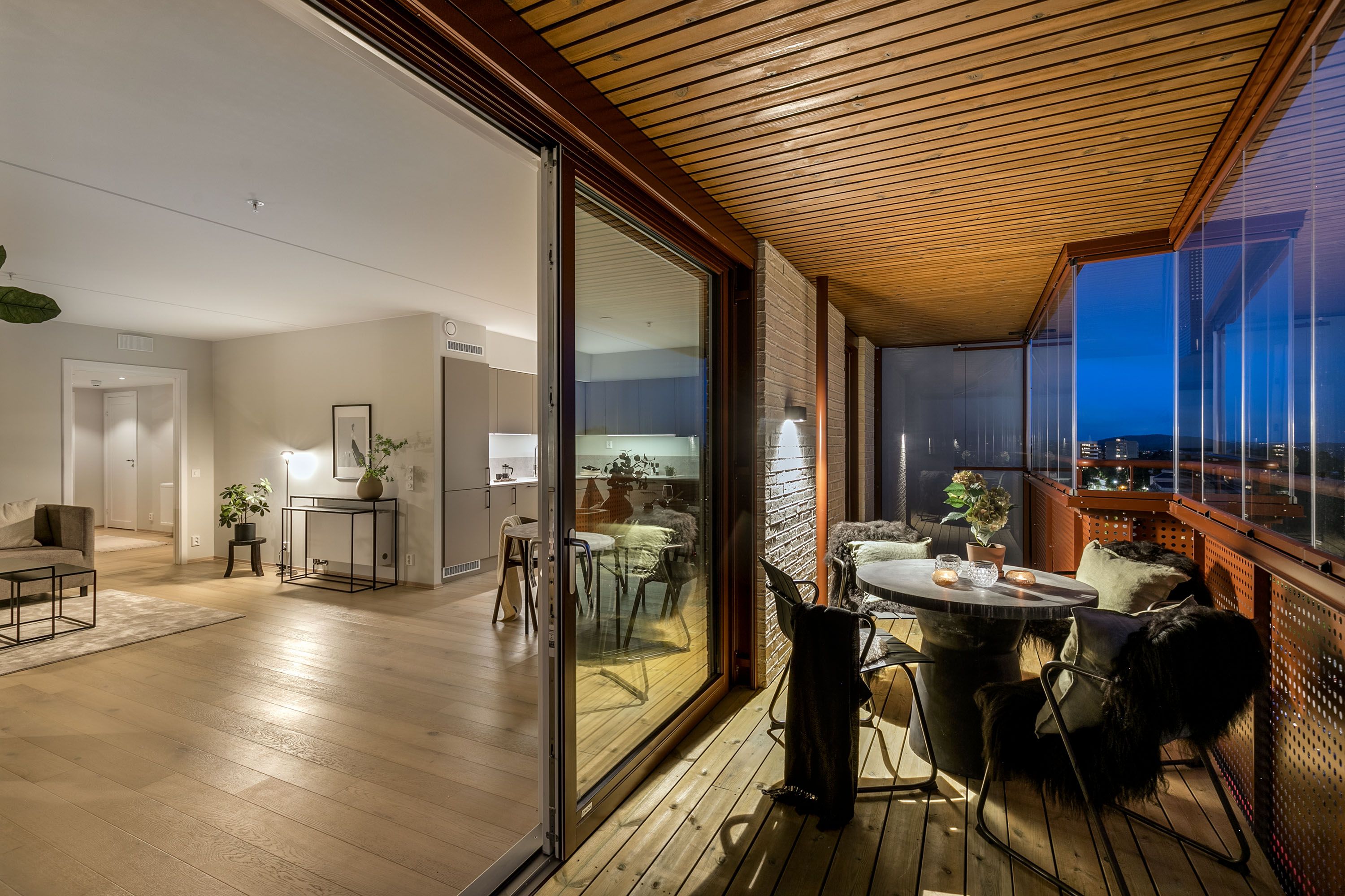 Bilde av terrasse tatt på kvelden. Ser inn på kjøkken og spisestua gjennom balkongdøra.