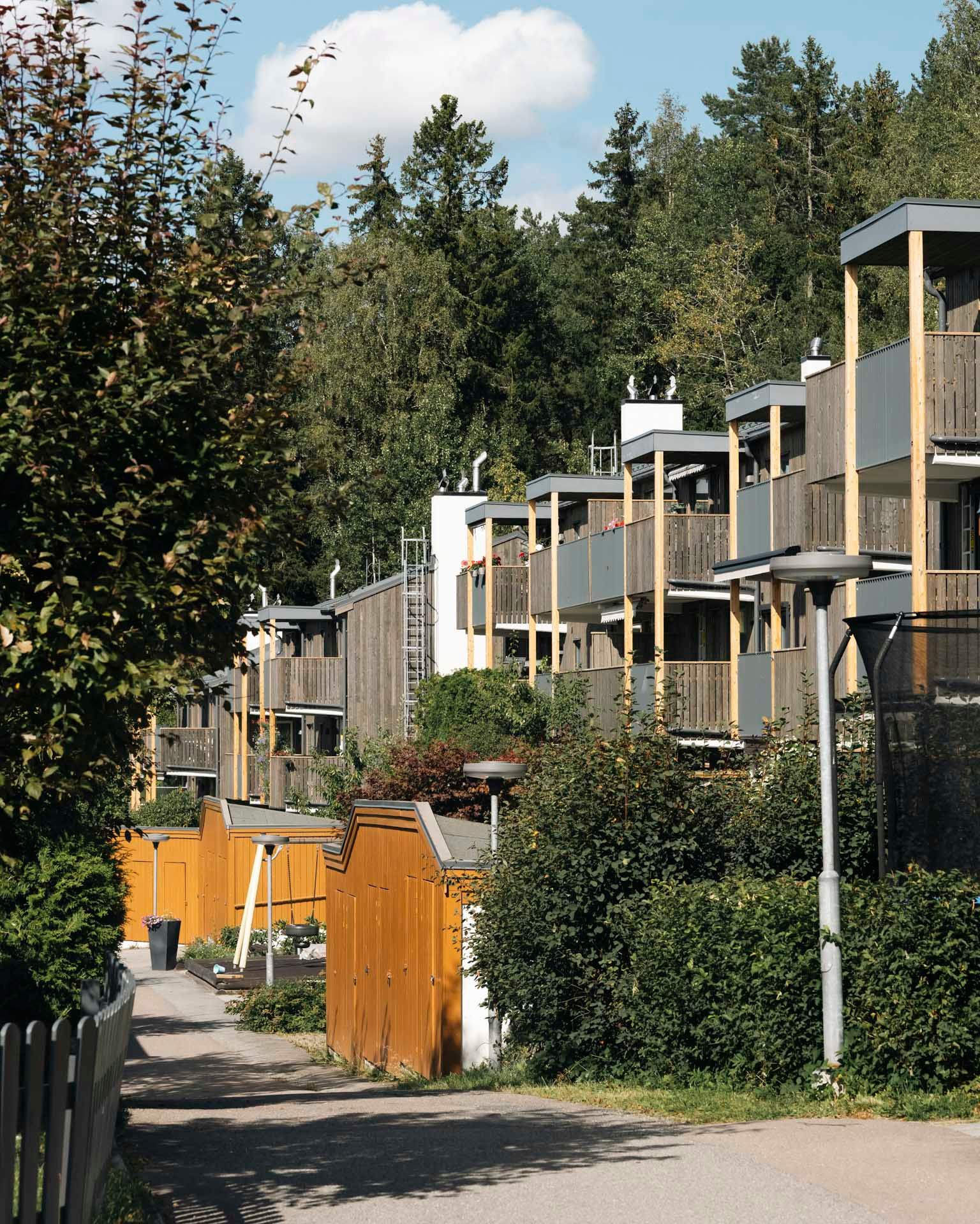 Rekke med moderne leilighetsbygg med nye fasader og balkonger, omgitt av grøntområder og trær på en solrik dag.