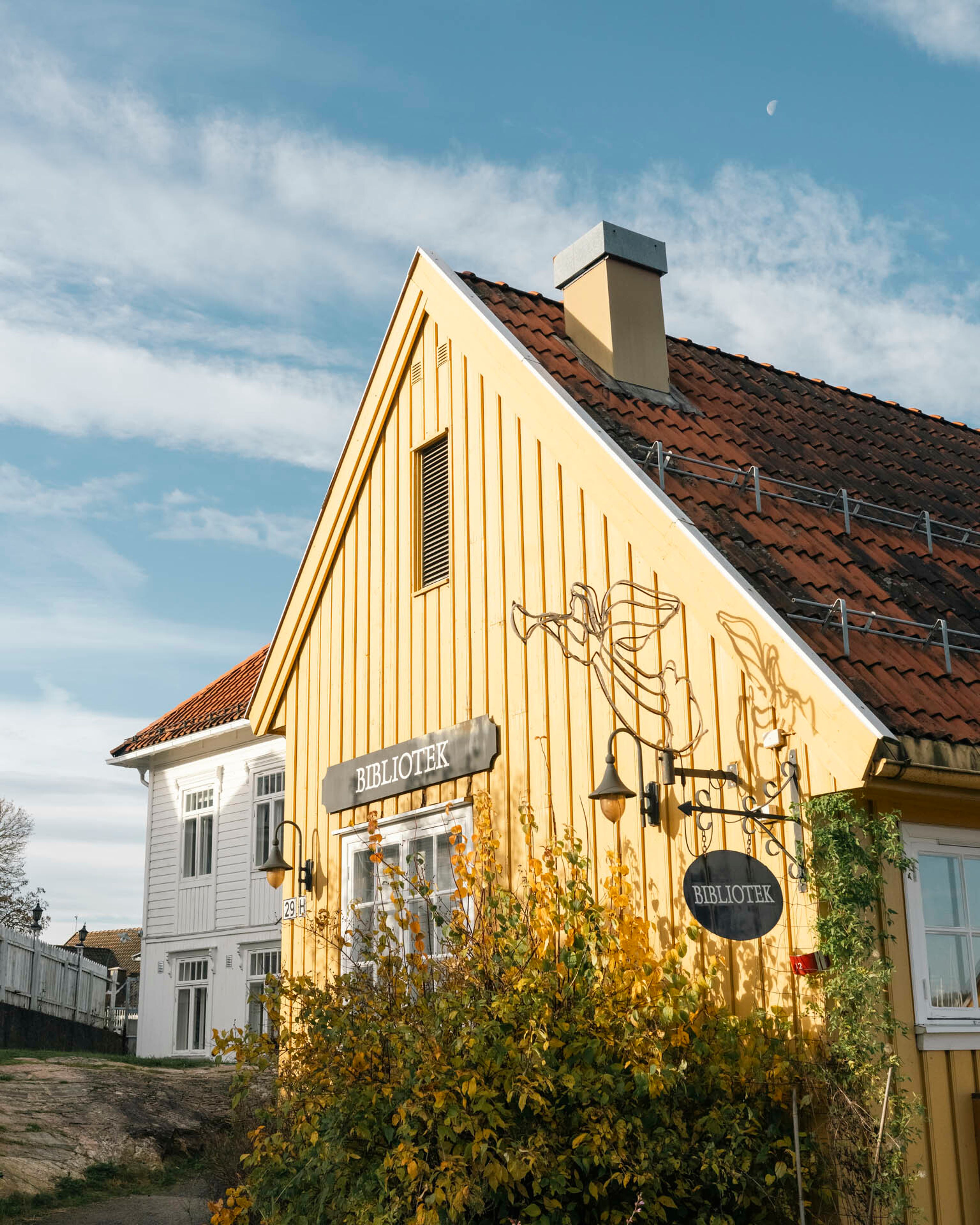 Foto av et gult trehus med skilt hvor det står "bibliotek", i Son.