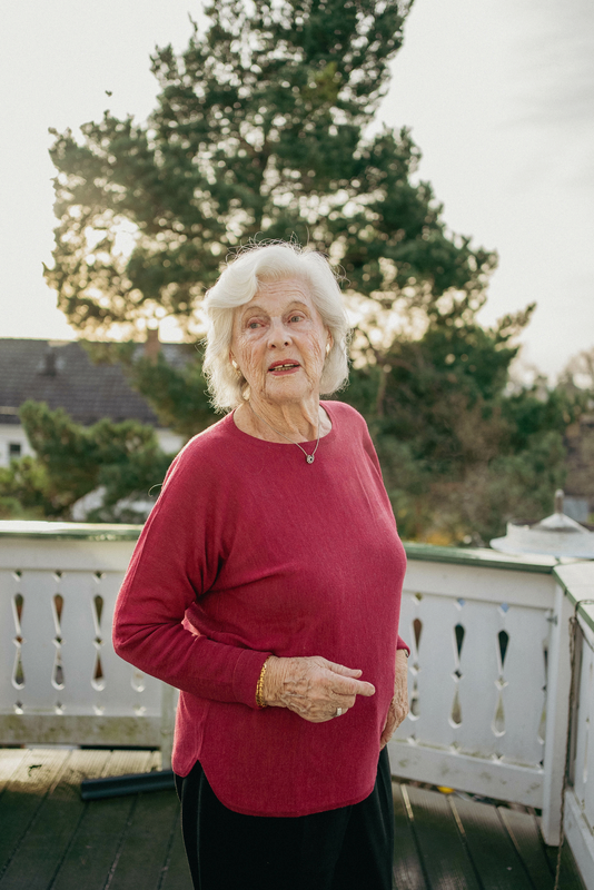 Unni står ute på verandaen sin i en rød overdel og ser mot kameraet