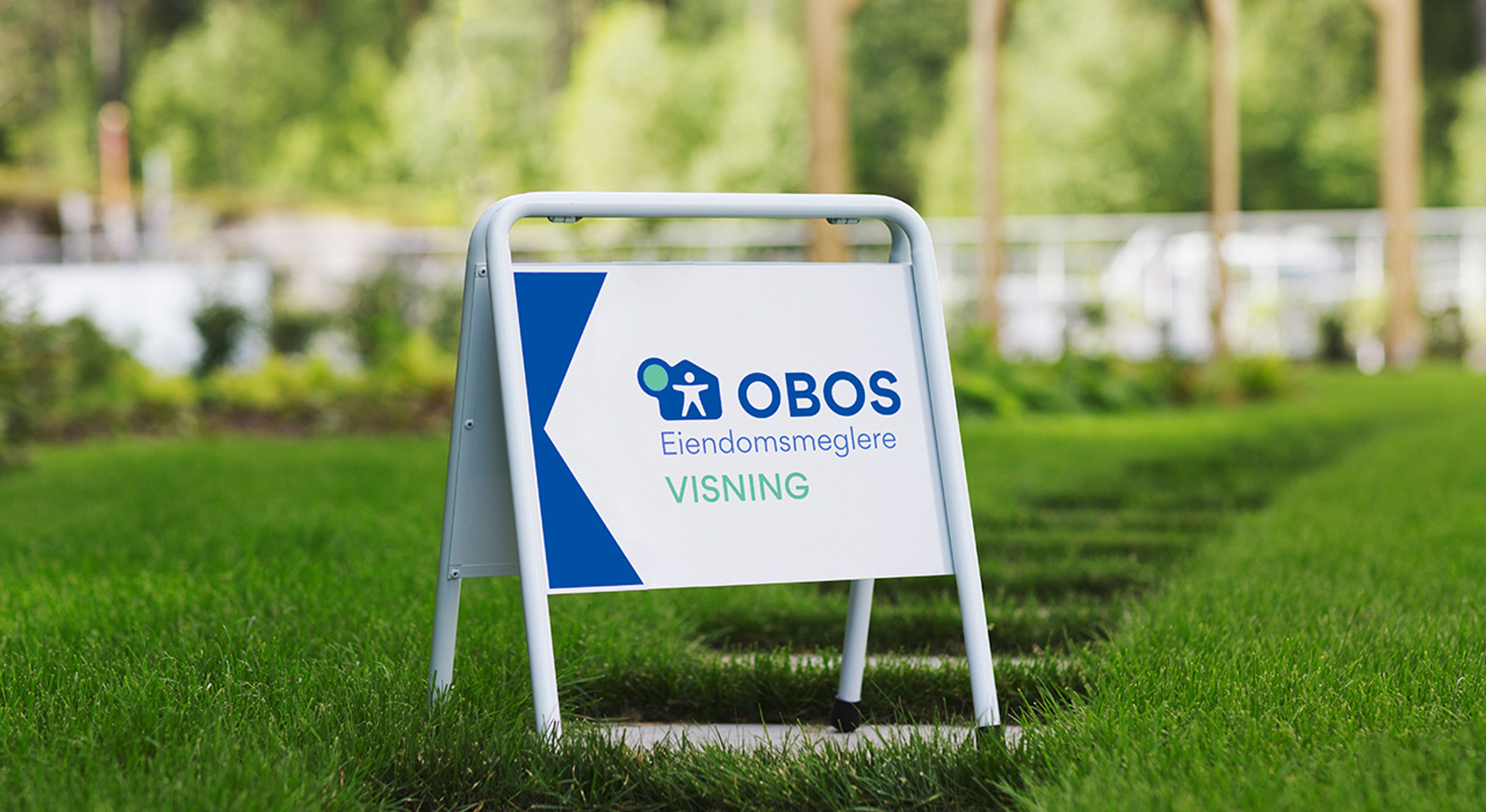 Et av visningsskiltene til OBOS Eiendomsmeglere på en gressplen.