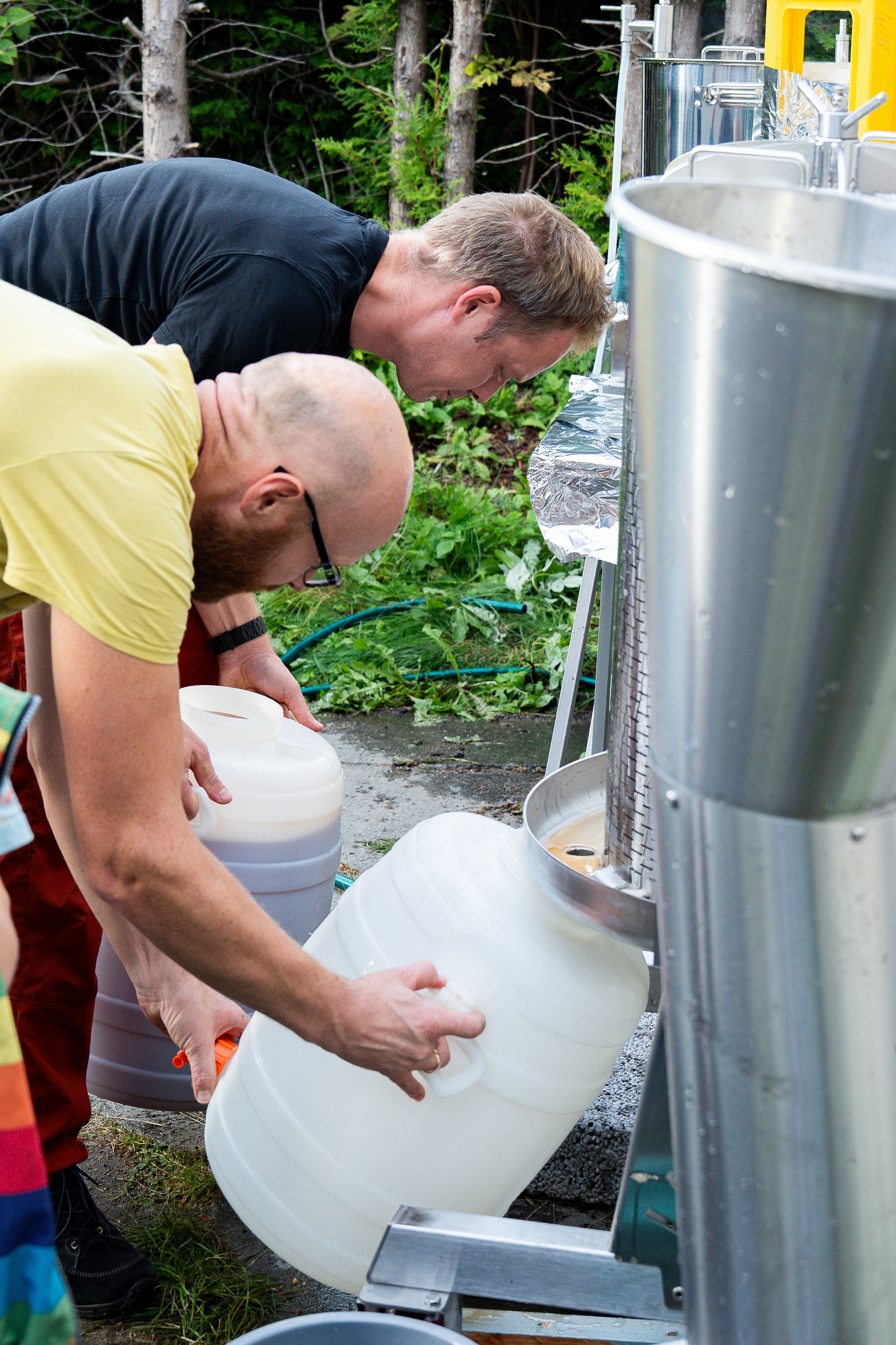 To menn står bøyd over en eplepresse og arbeider